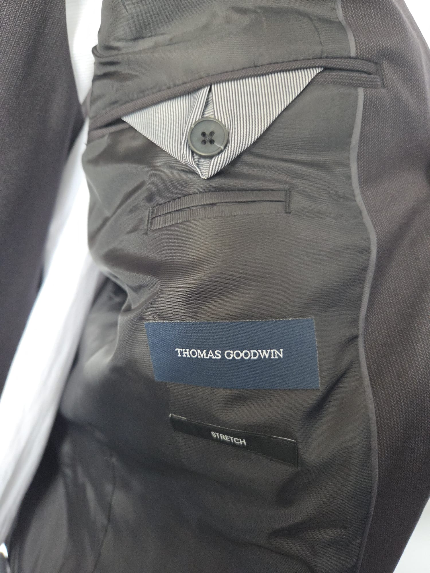 Inside lining of Thomas Goodwin black suit showing brand label, button pocket , and stretch fit label.