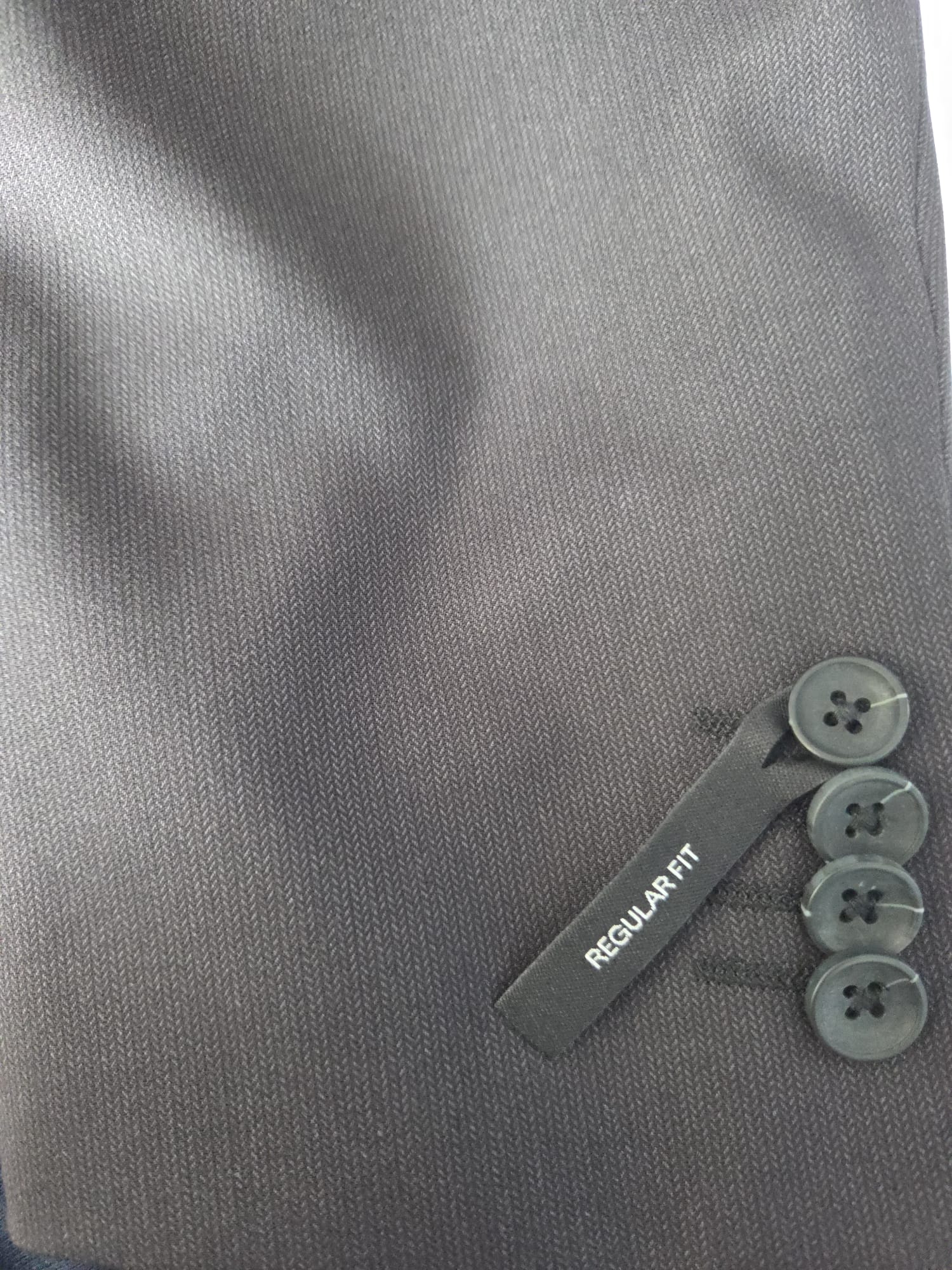 Sleeve close-up with four buttons showing fine herringbone texture and regular fit tag.