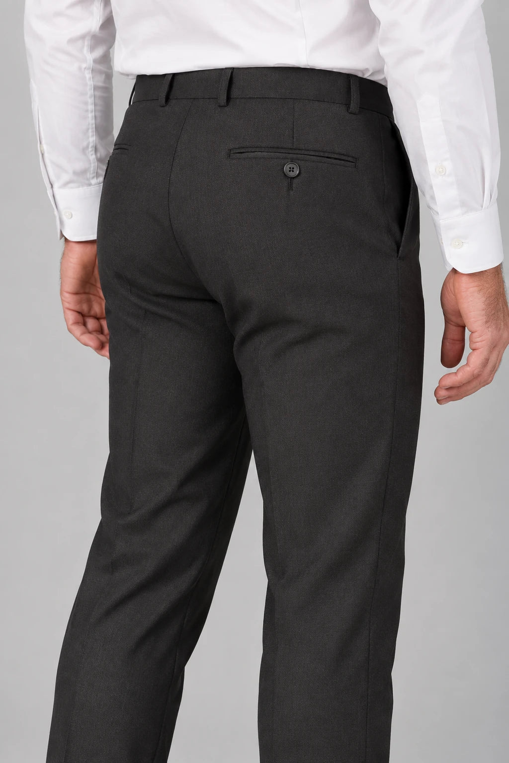 Rear view of a person wearing dark charcoal black dress pants with a white dress shirt, showing the back pocket and waistband details against a studio background.