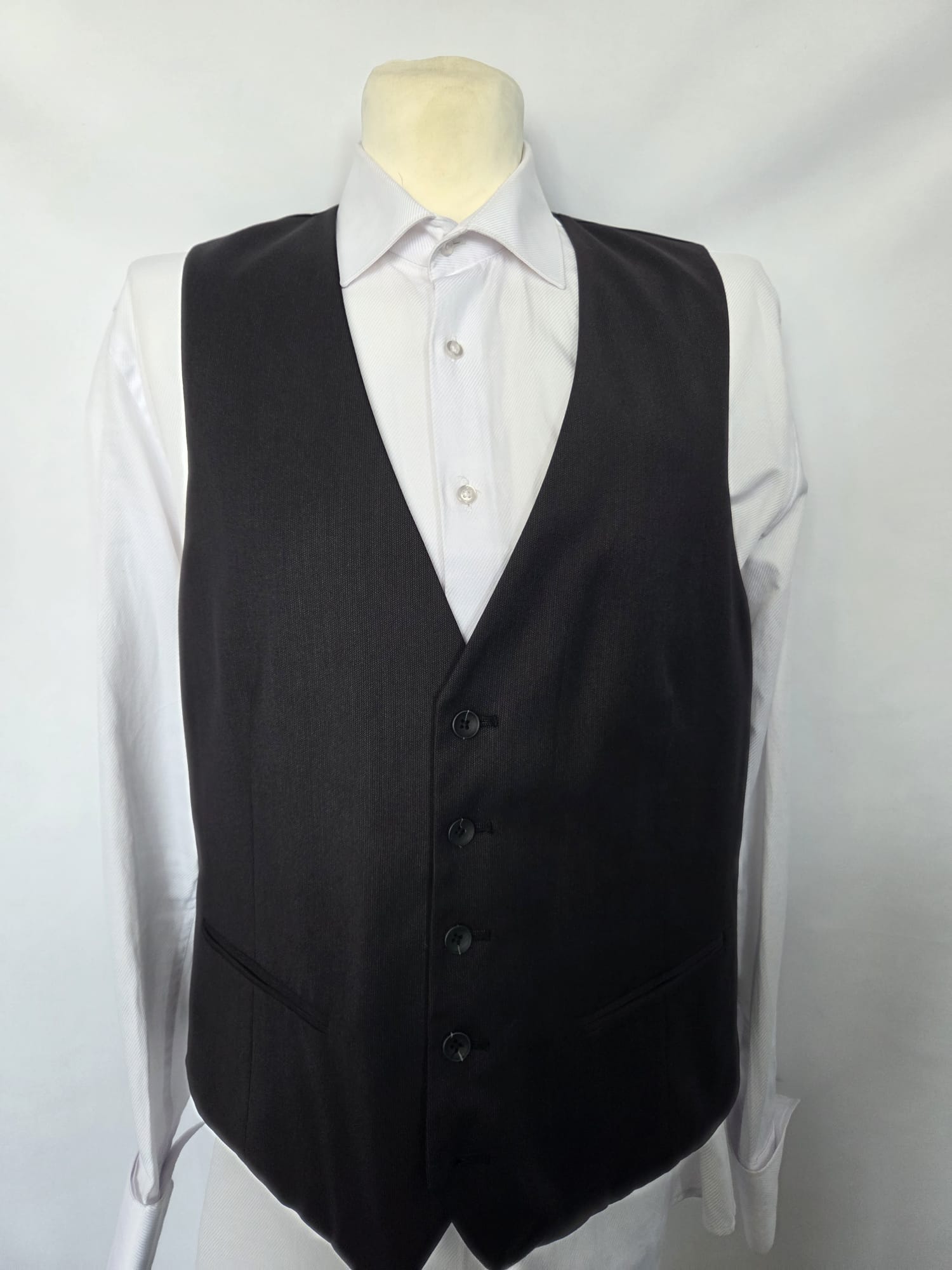Front view of black Thomas Goodwin waistcoat with four buttons, two welt pockets, worn over a white shirt.