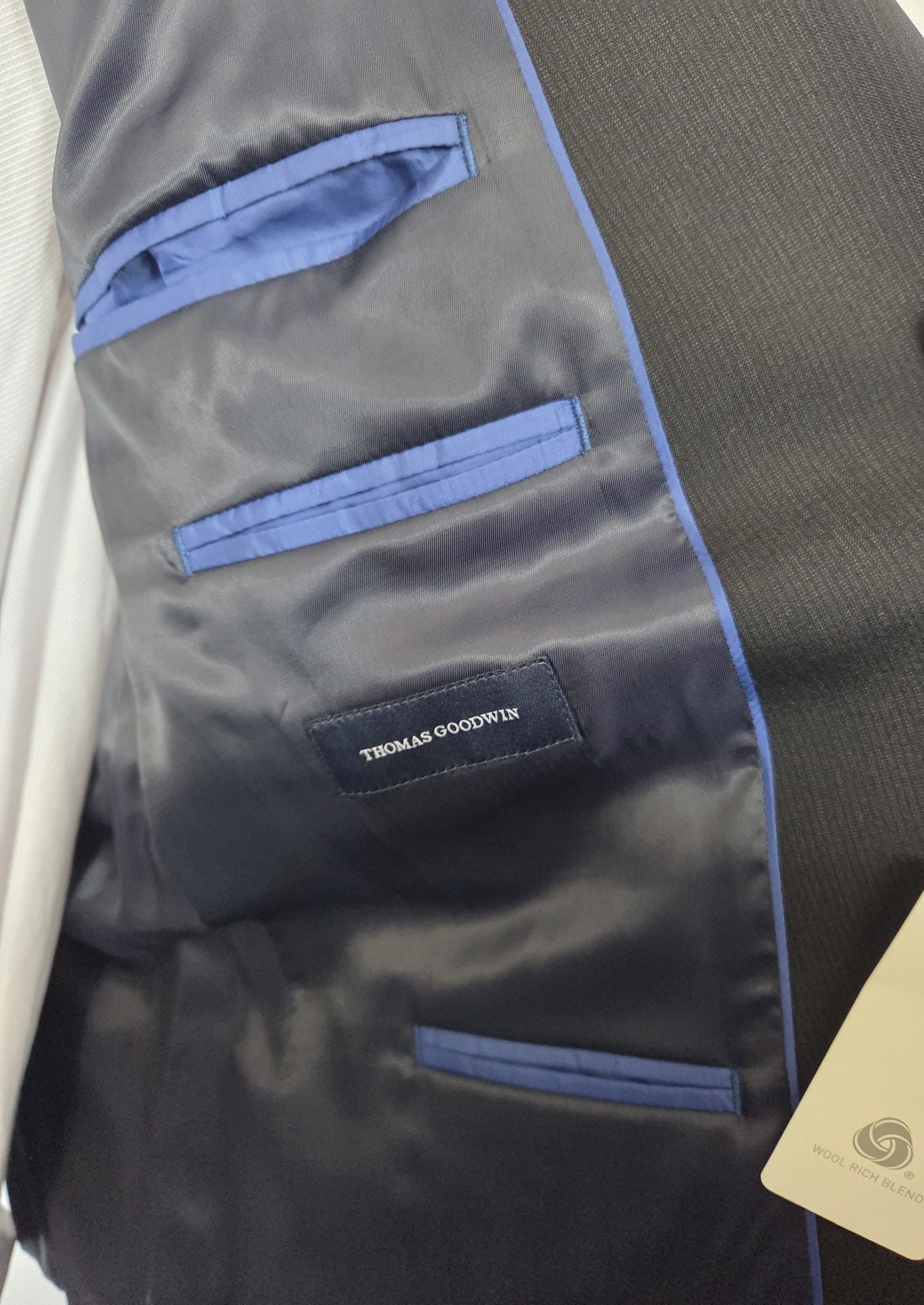Inside lining detail of Thomas Goodwin black suit showing navy piping and internal pockets with brand label.