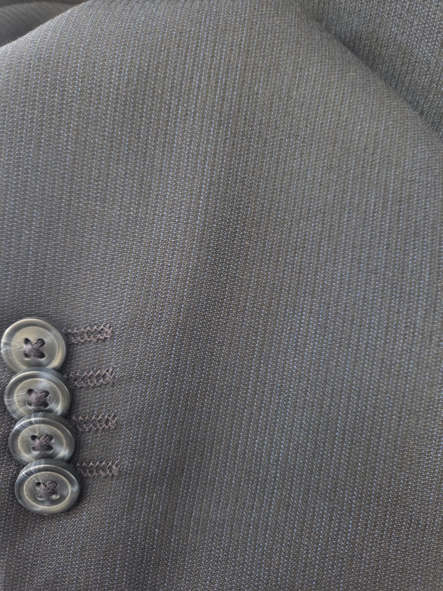 Close-up of dark navy virgin wool fabric with subtle micro-stripe texture and four-button cuff.