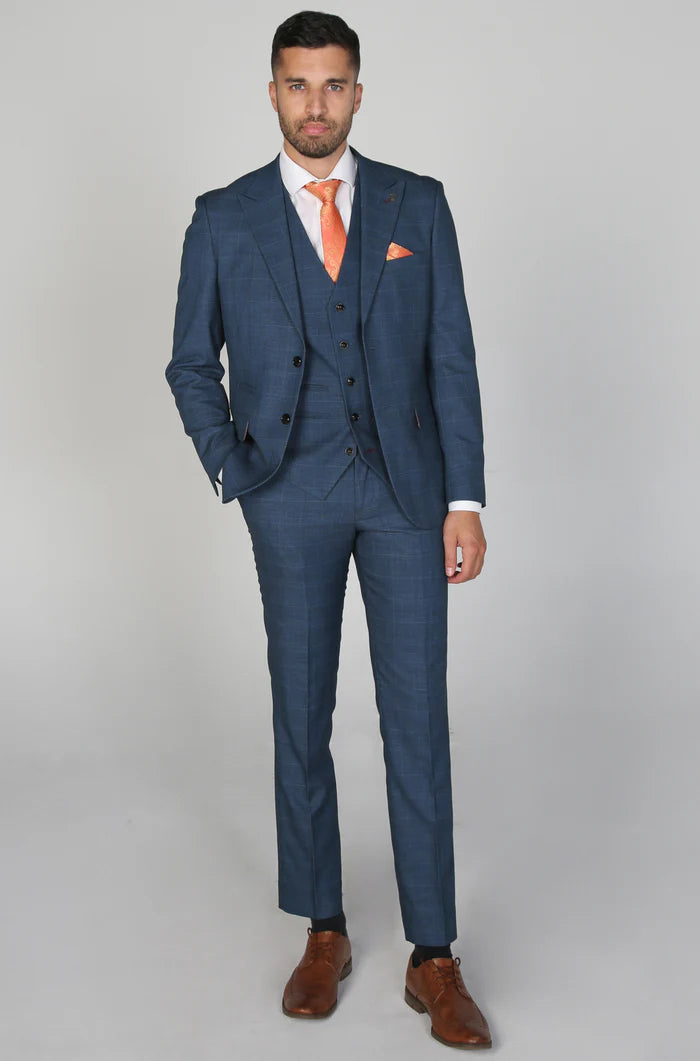 Full-body view of a man wearing a navy check three-piece suit styled with an orange paisley tie and brown shoes.