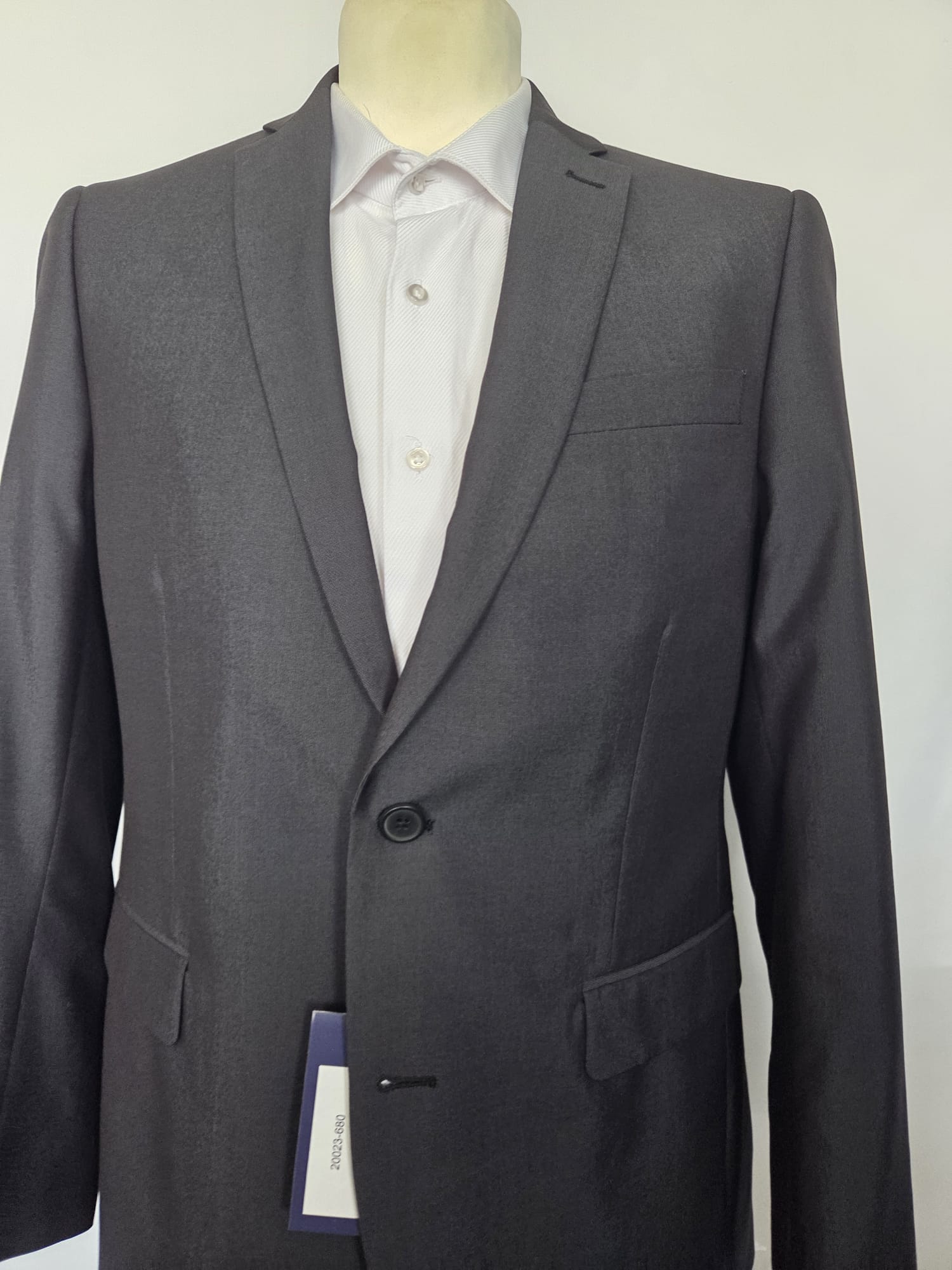 Close-up of dark grey suit jacket front with one-button fastening and clean tailoring.