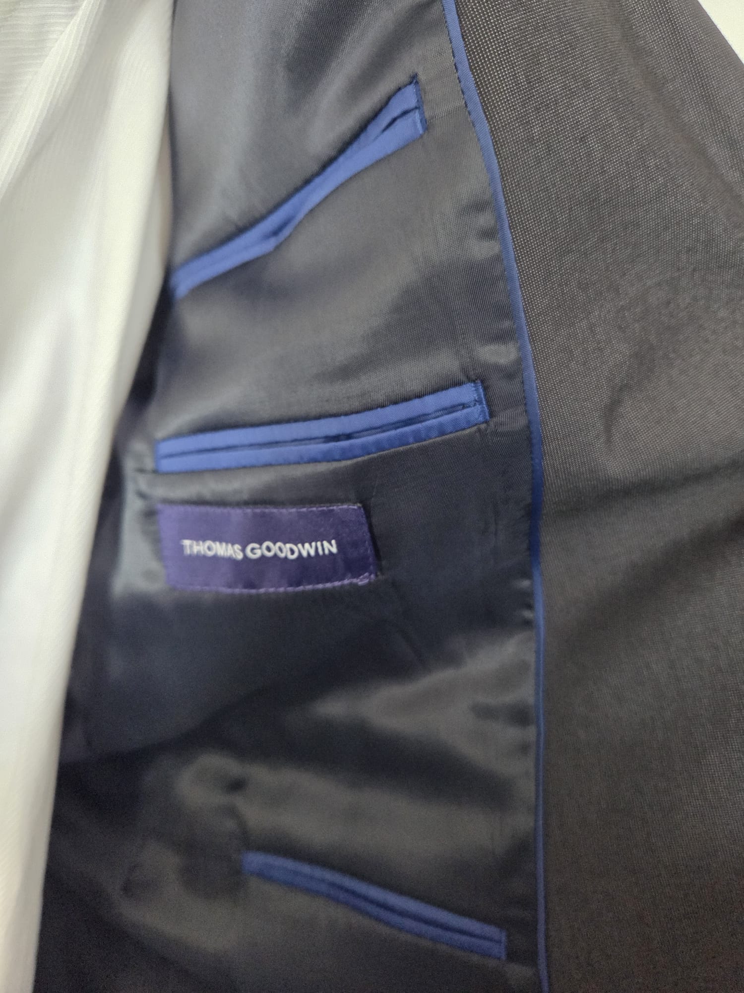 Inside lining of dark grey suit jacket with blue piping and Thomas Goodwin label.