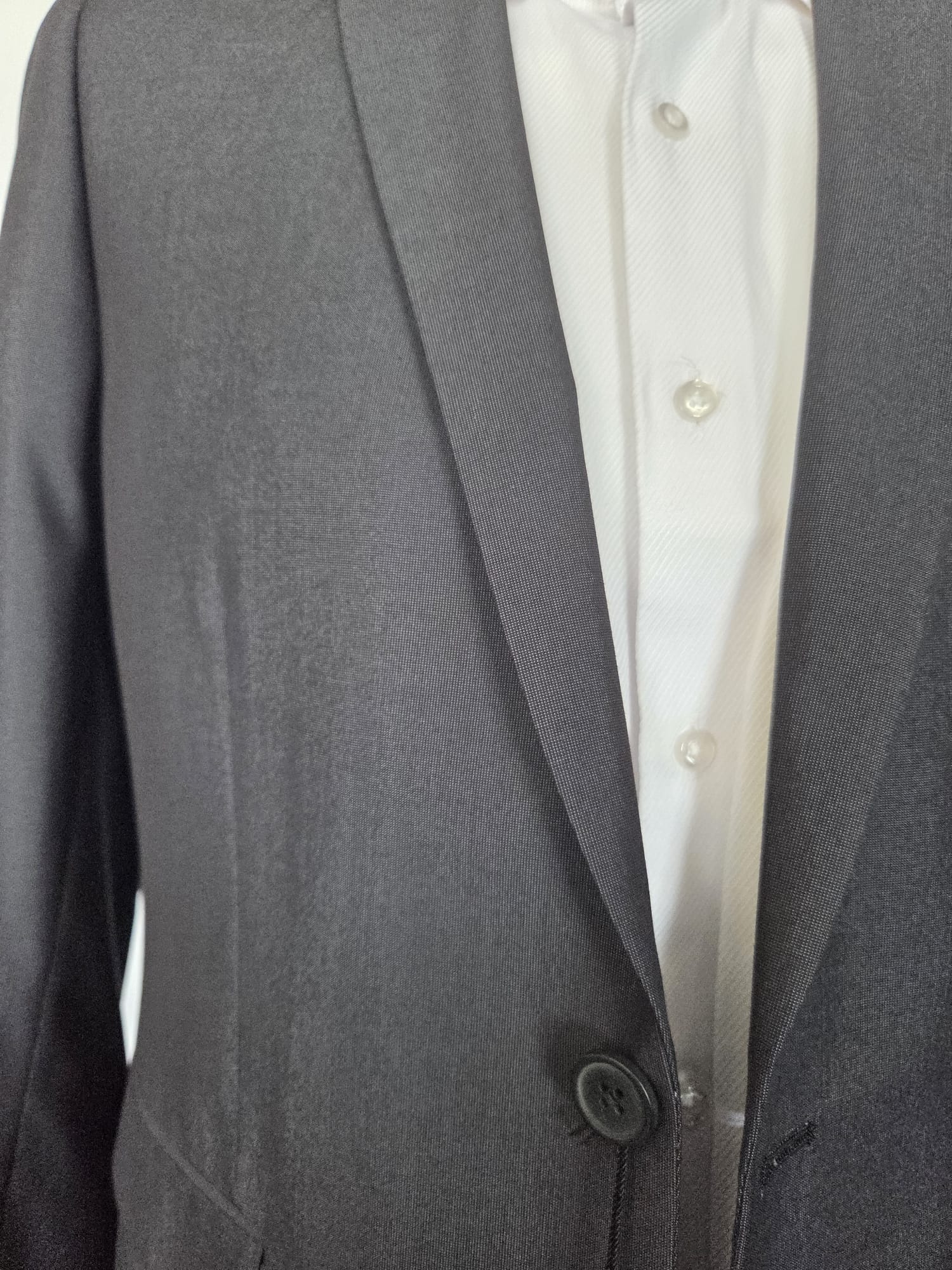 Close-up of dark grey suit lapel and single front button showing smooth micro-weave fabric.