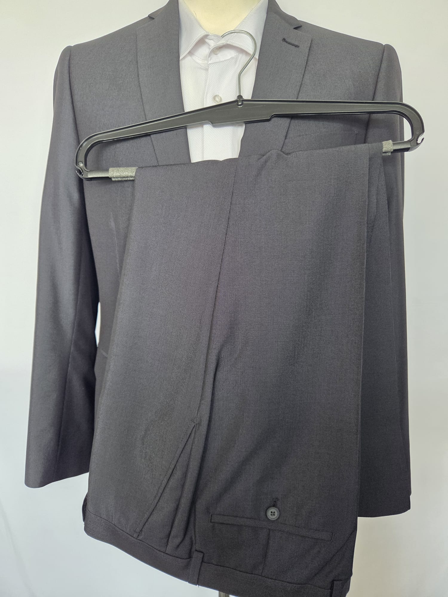 Dark grey two-piece suit jacket with matching trousers on hanger.