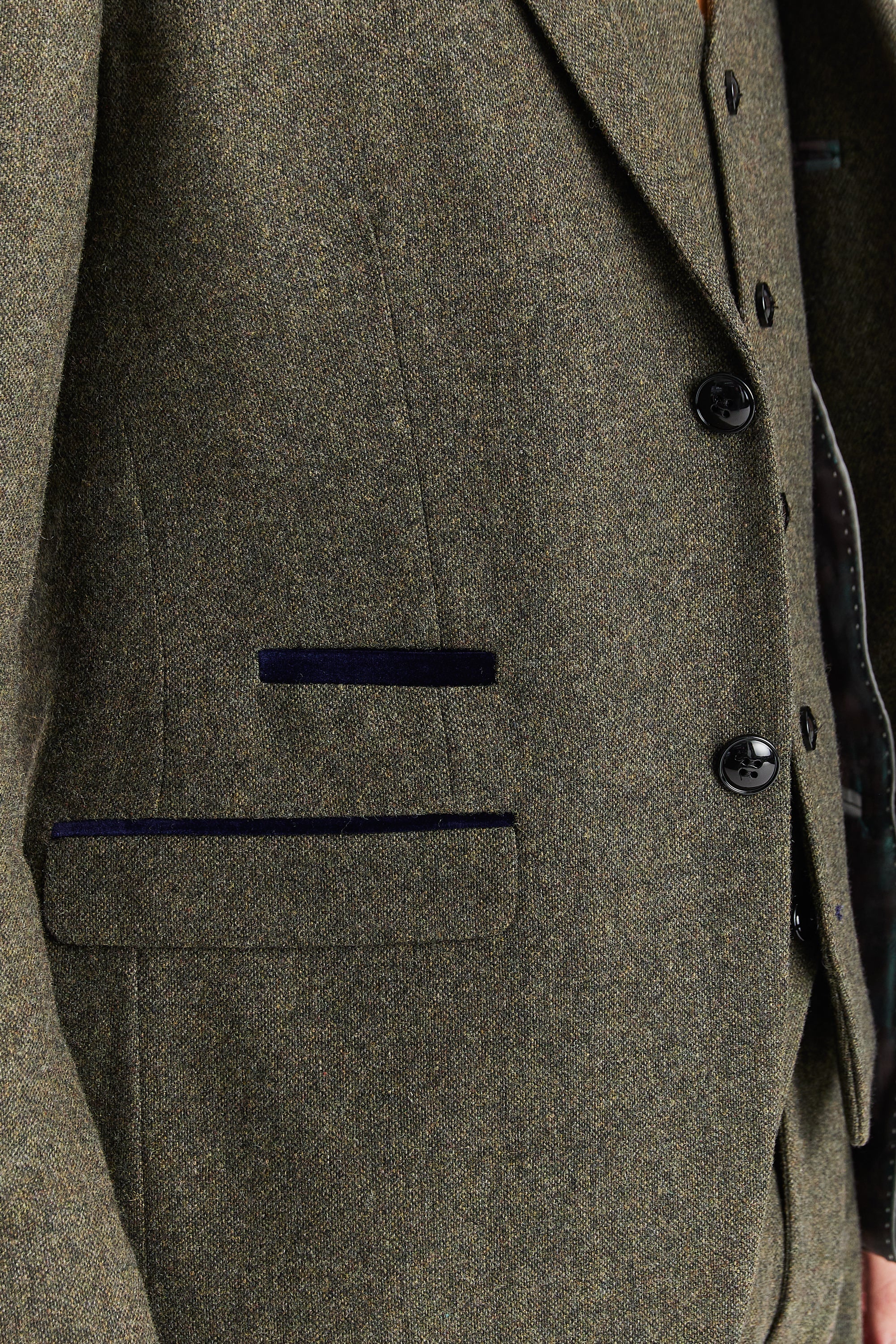 Close-up view of the green tweed blazer showing the textured woven tweed surface, dark buttons, front flap pocket and navy trim detail.