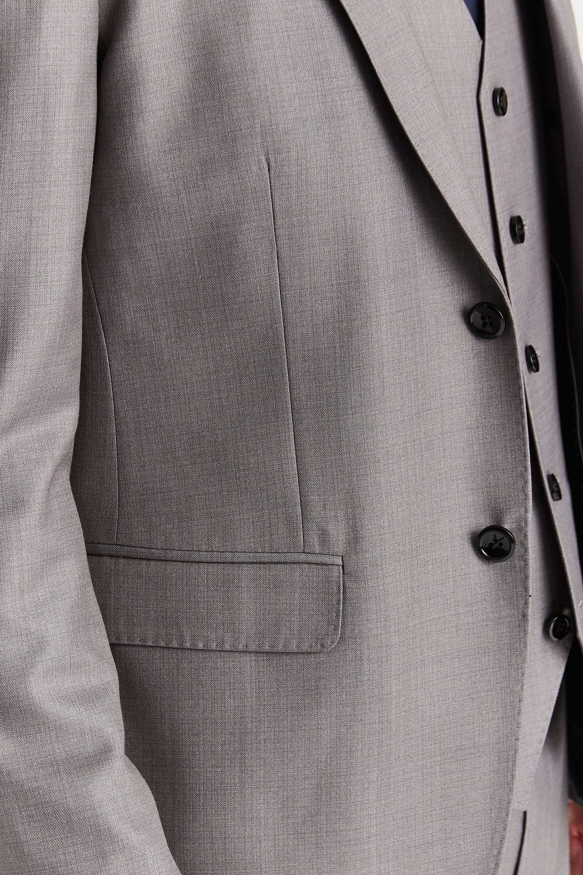 Close-up view of the grey blazer showing the fine woven surface, front flap pocket and black buttons.