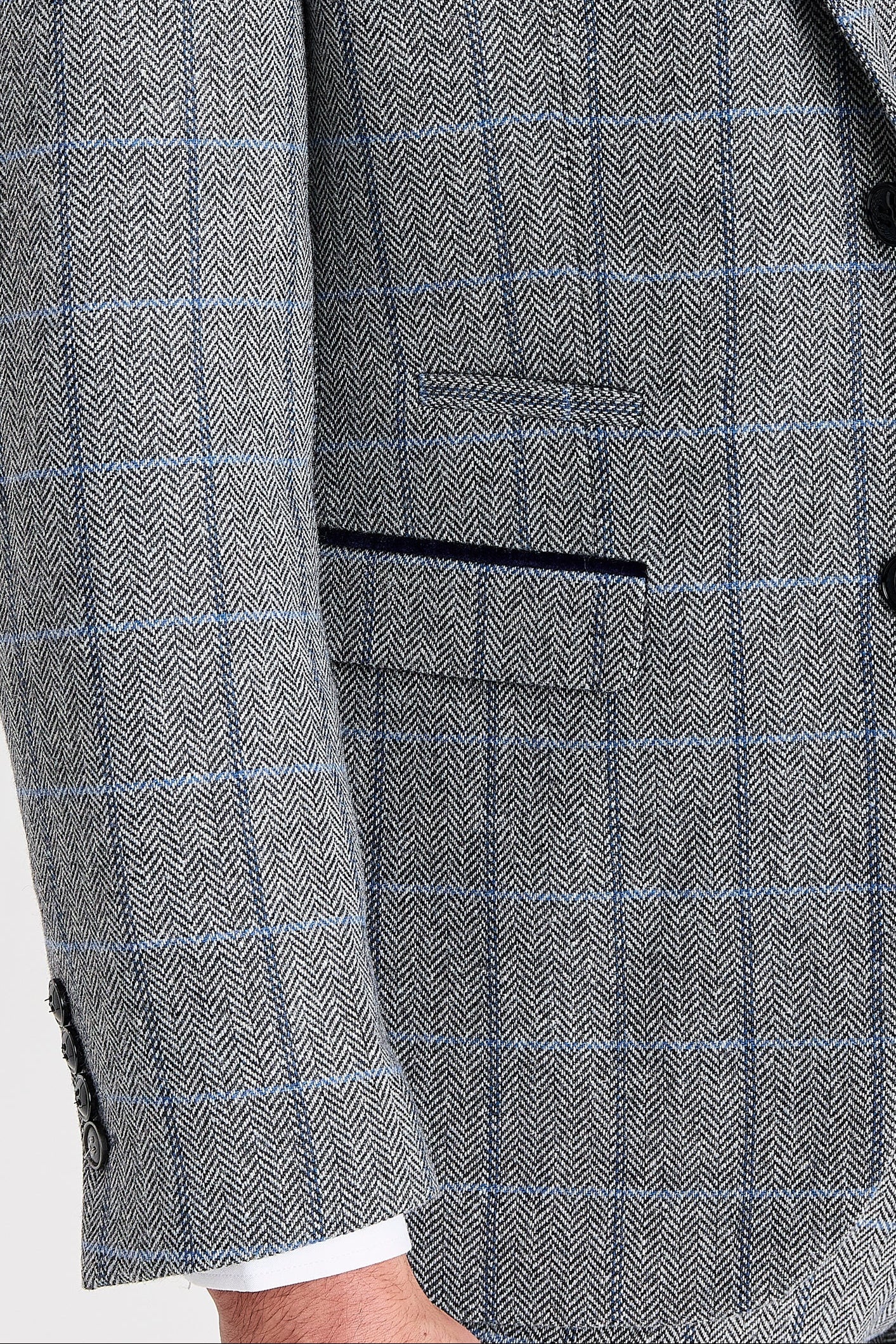 Close-up view of the grey herringbone tweed check blazer showing the woven texture, windowpane check, front flap pocket, upper pocket and dark suede trim.