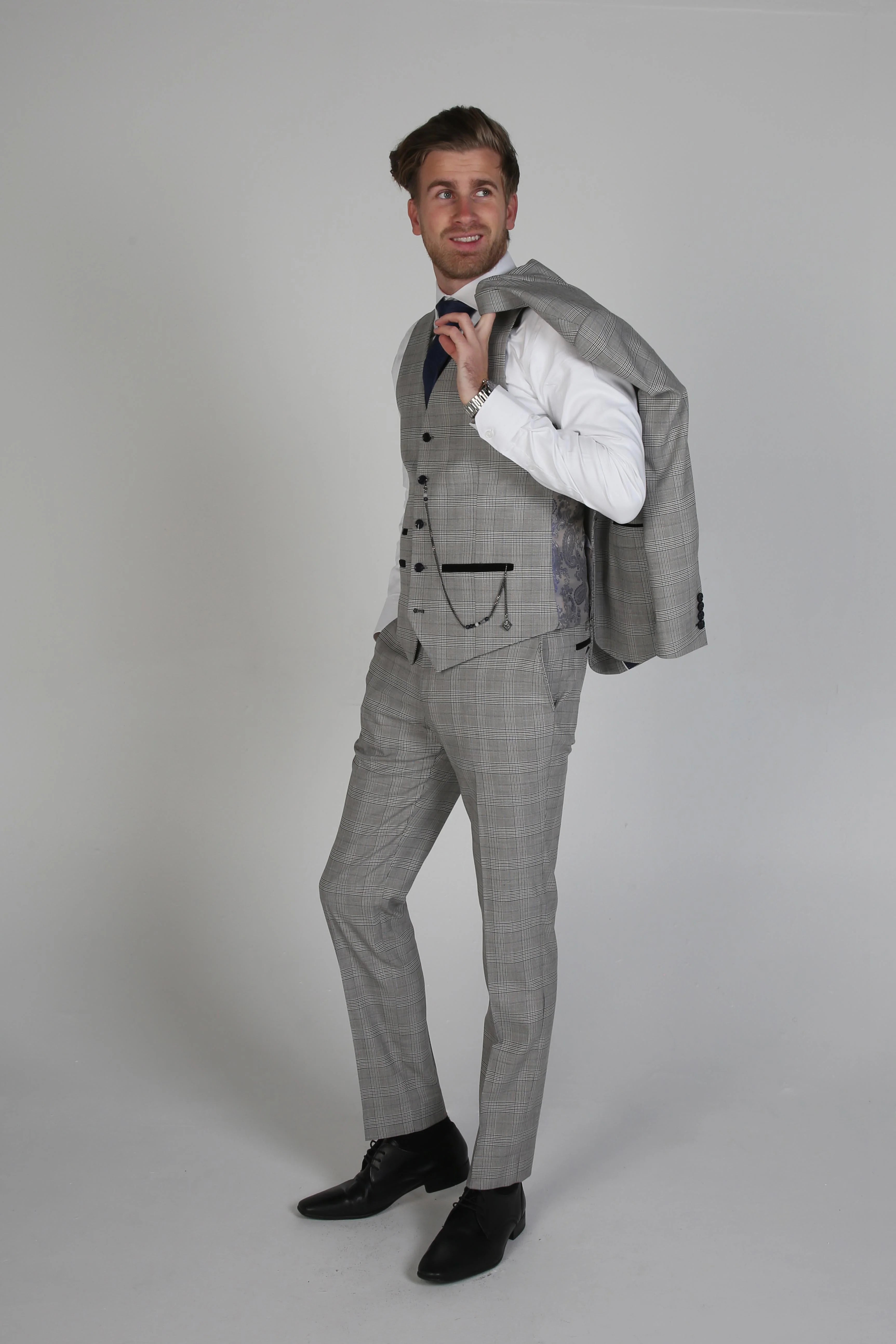 Man wearing a Hugo grey checkered three-piece suit with a white dress shirt, holding the jacket over his shoulder.