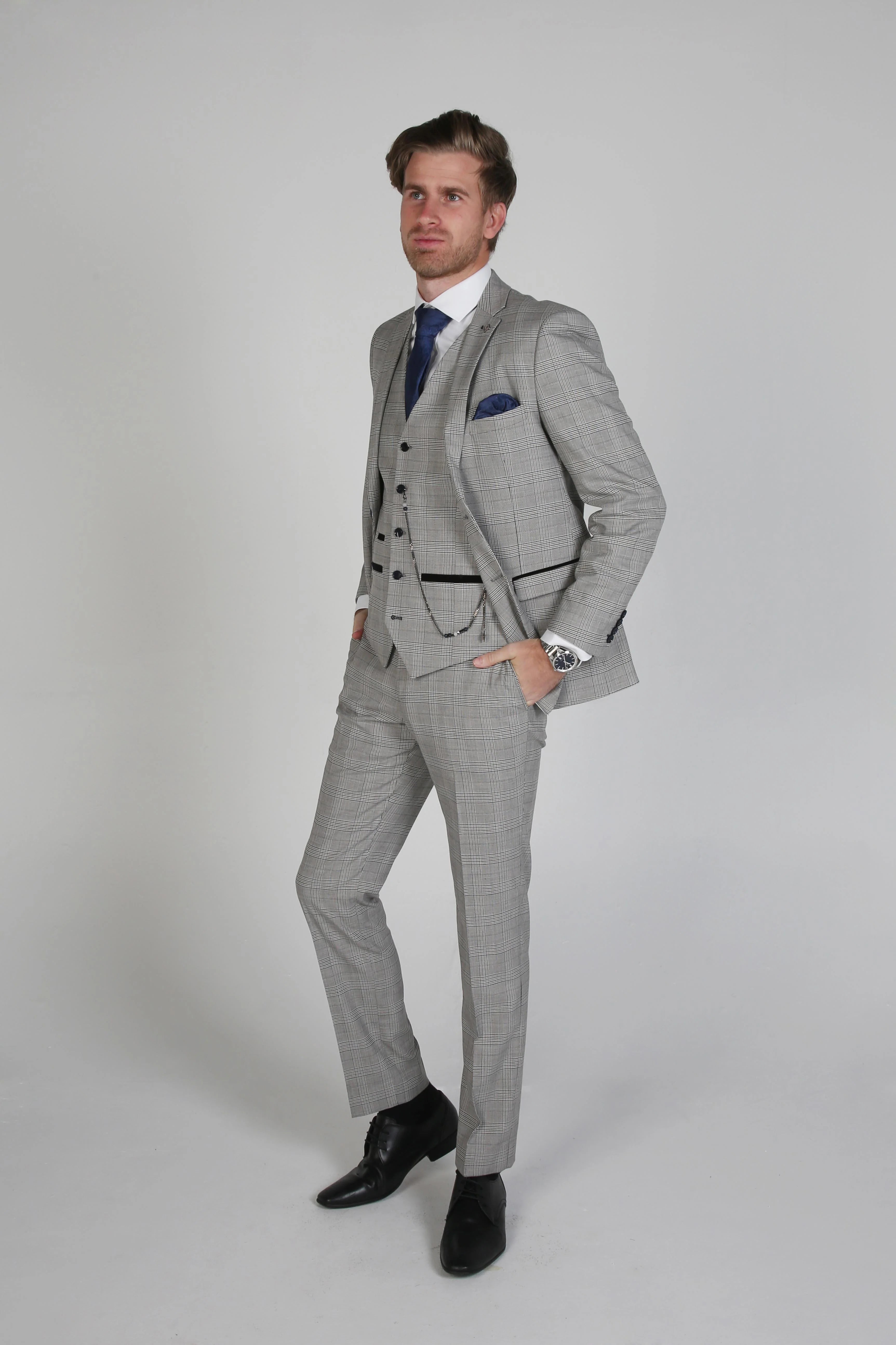  Side view of a man in a Hugo grey checkered three-piece suit with a white dress shirt and blue tie, hands in pockets.