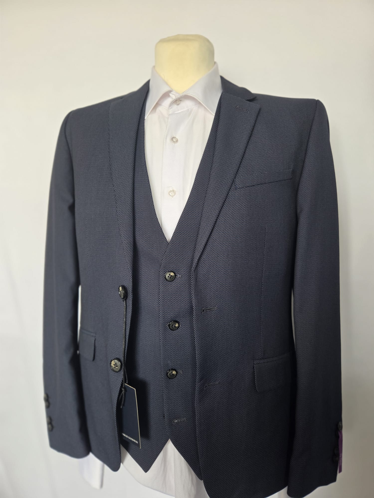 Angled front view of navy birdseye weave three-piece suit with white shirt.