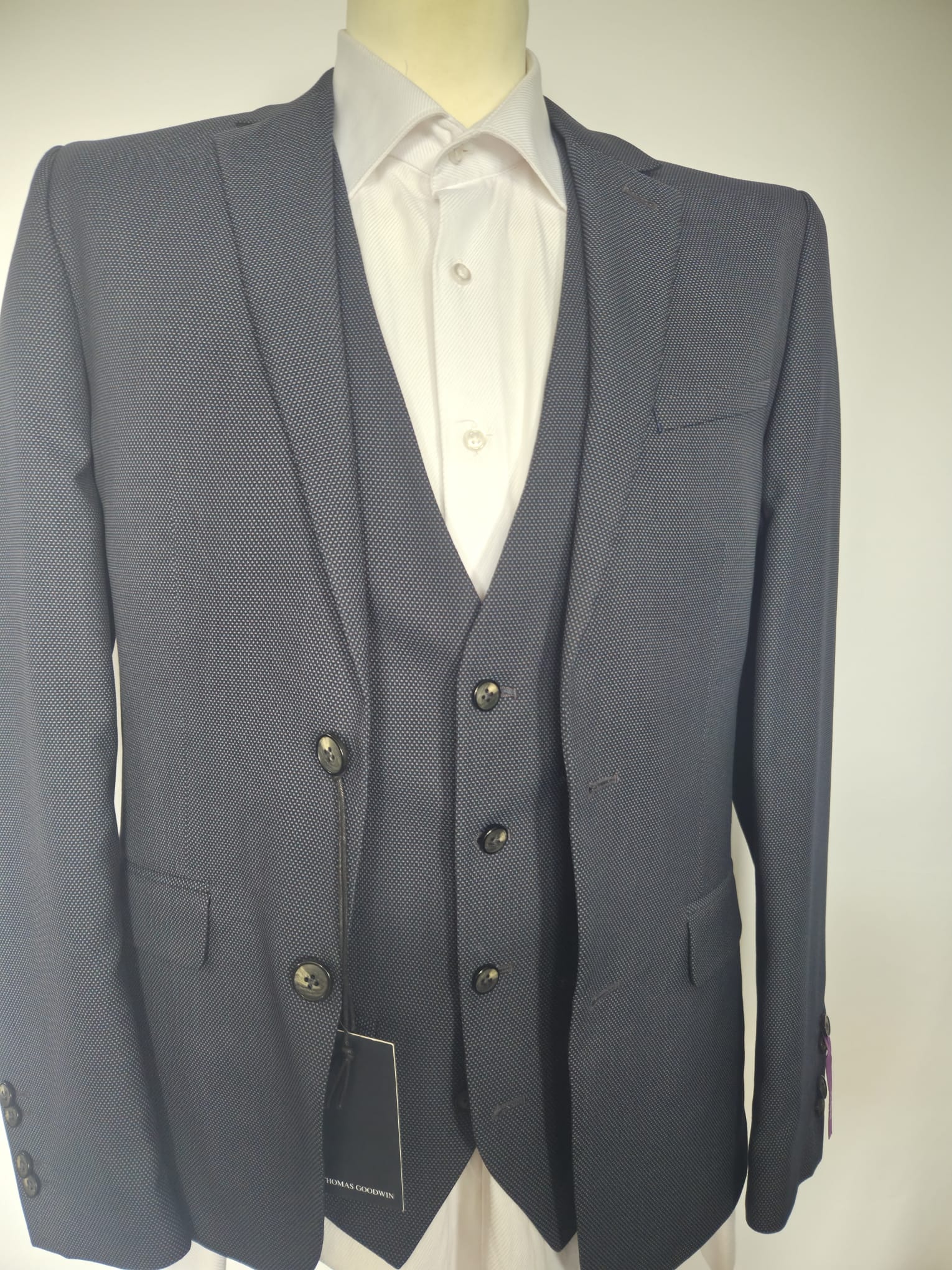 Close-up front view of navy birdseye weave suit jacket and waistcoat with black buttons.