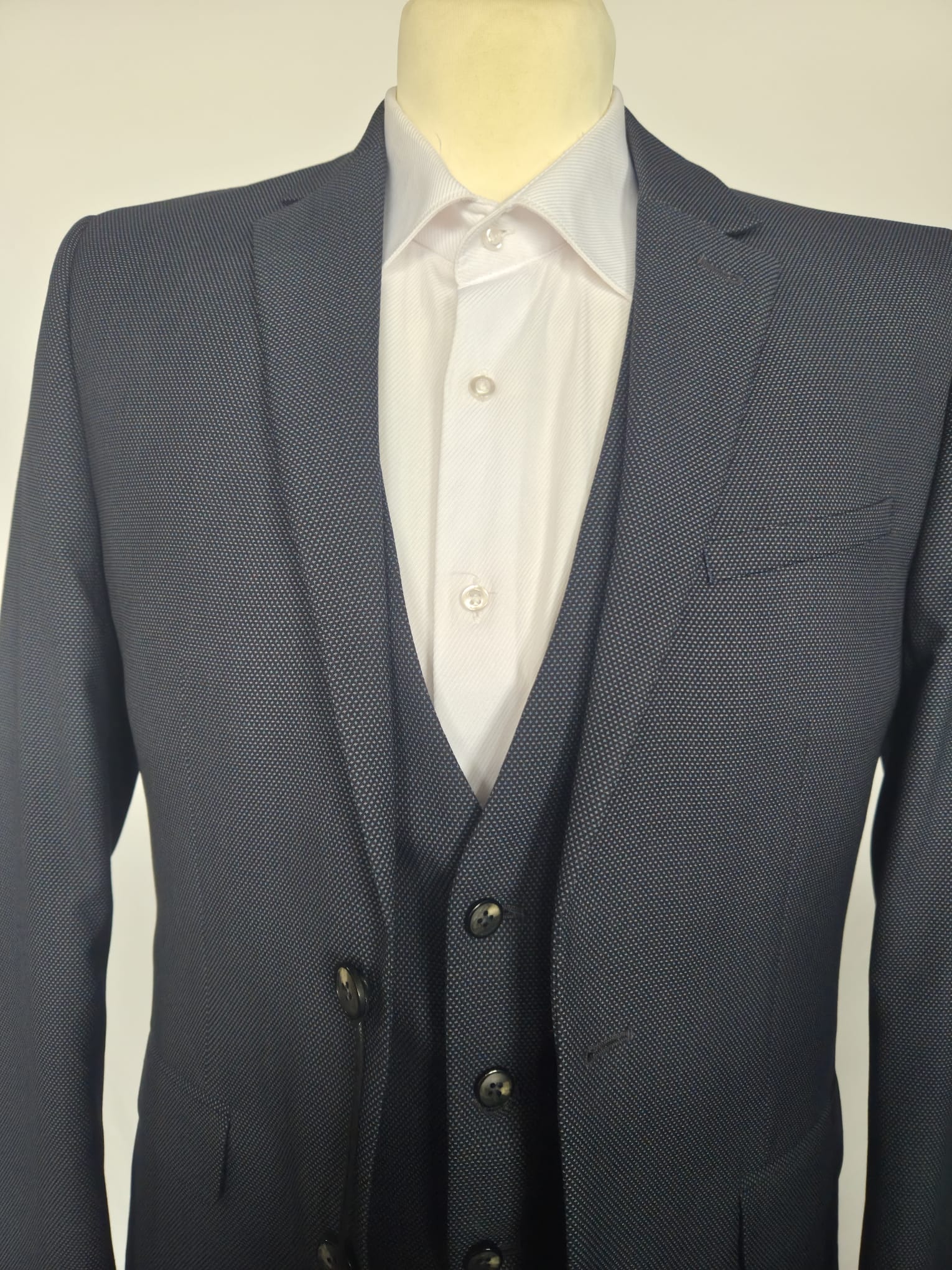 Front view of navy birdseye weave three-piece suit with jacket and waistcoat, paired with white shirt.