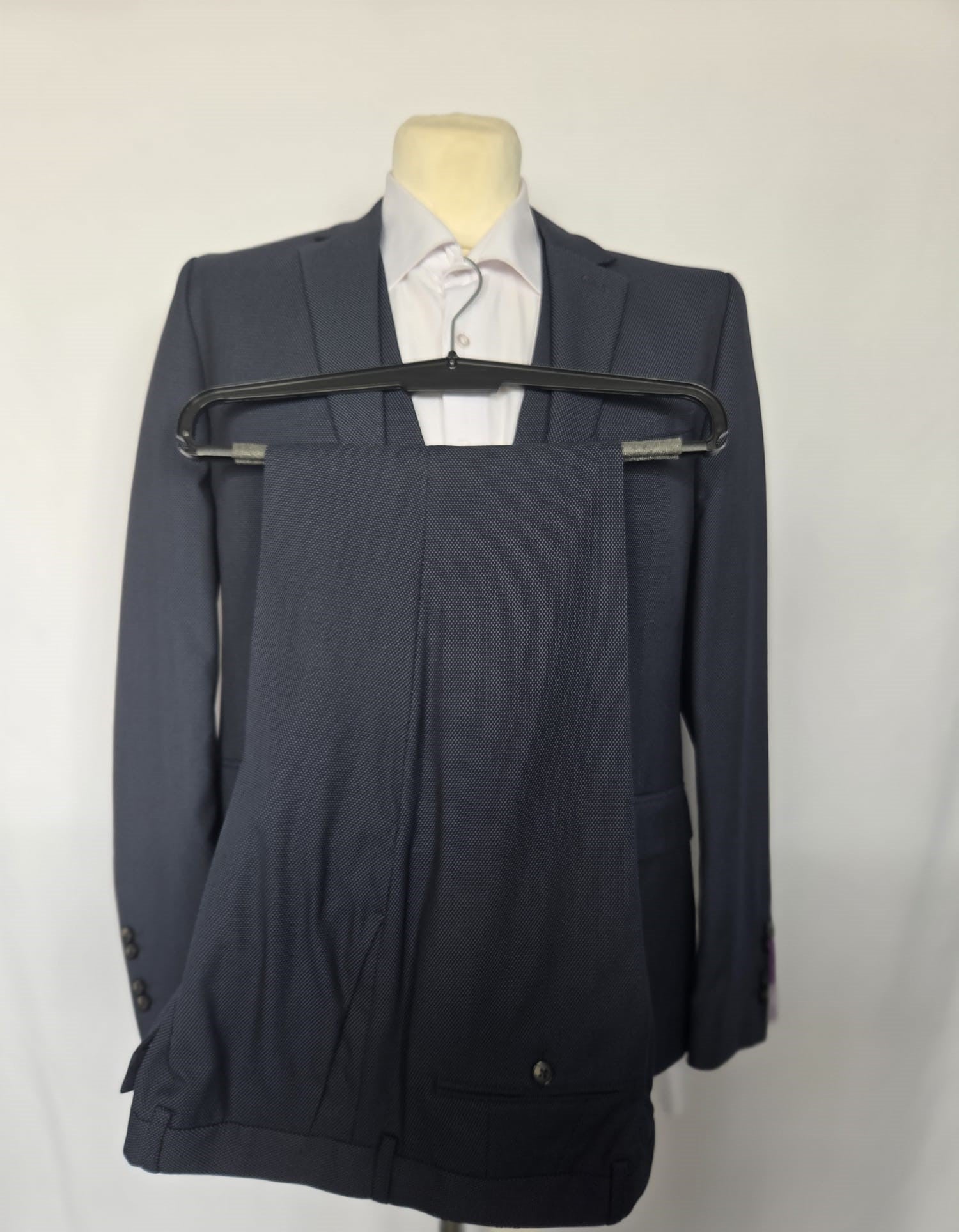 Navy birdseye weave three-piece suit with matching trousers displayed on hanger.
