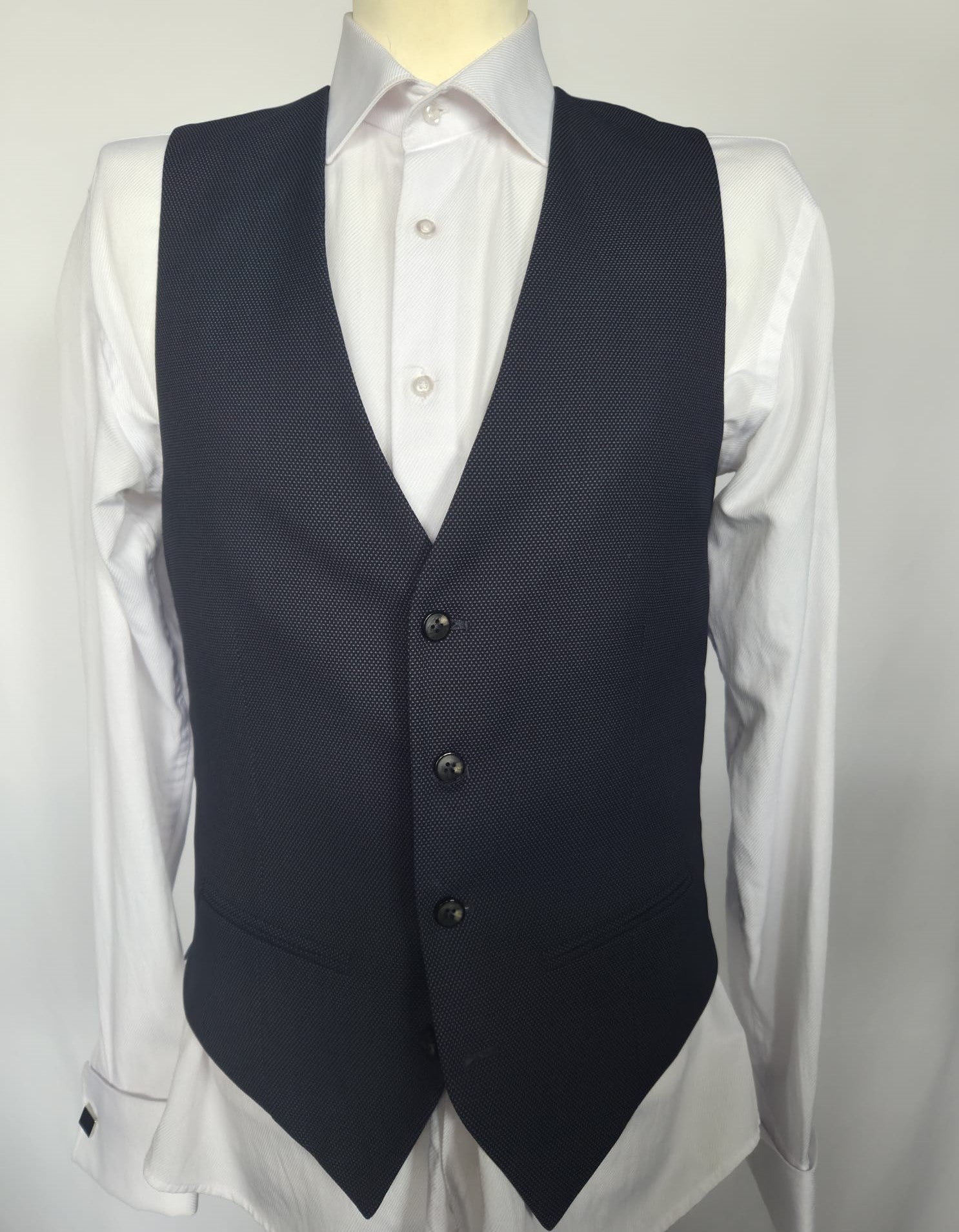 Front view of navy birdseye weave waistcoat with black buttons, worn over white dress shirt.
