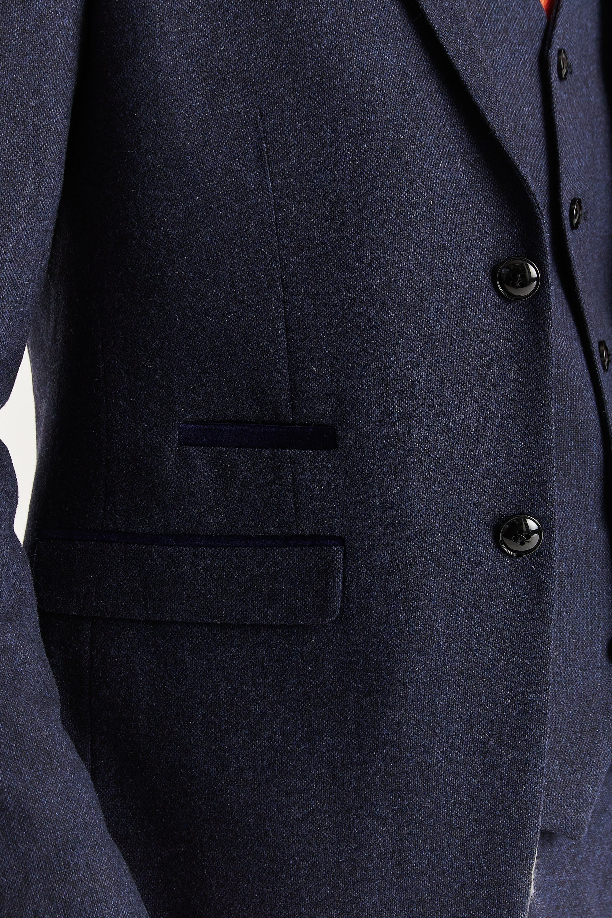 Close-up view of the navy tweed blazer showing the textured woven surface, black buttons, front flap pocket and dark trim detail above the pocket.