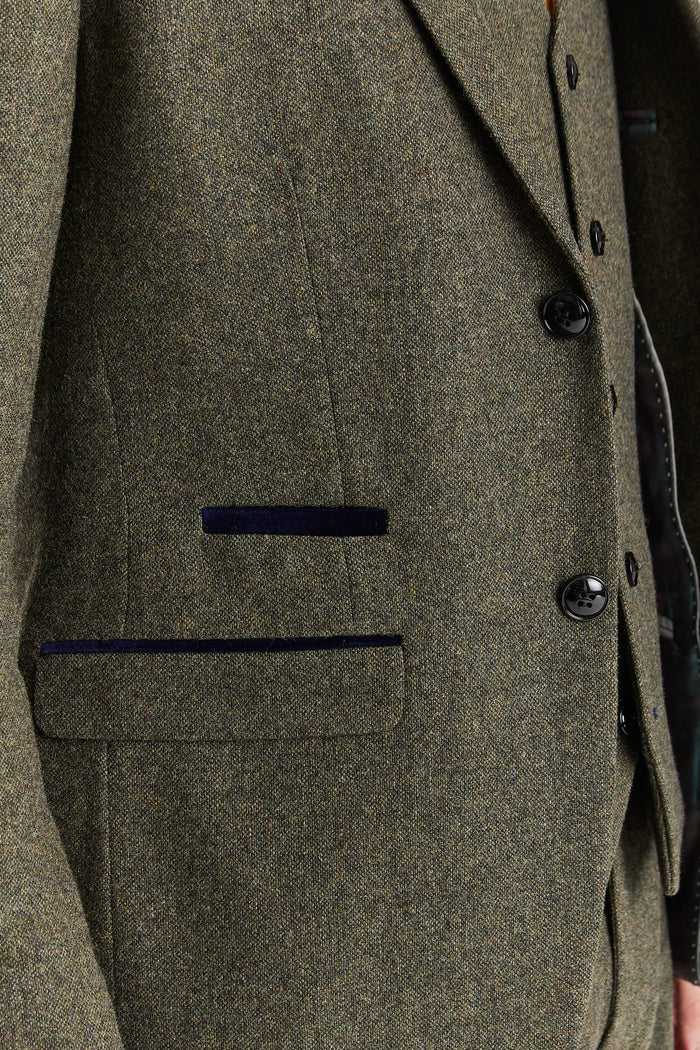 Close-up of Oscar green tweed suit jacket pocket and button detail highlighting textured fabric and dark trim.

