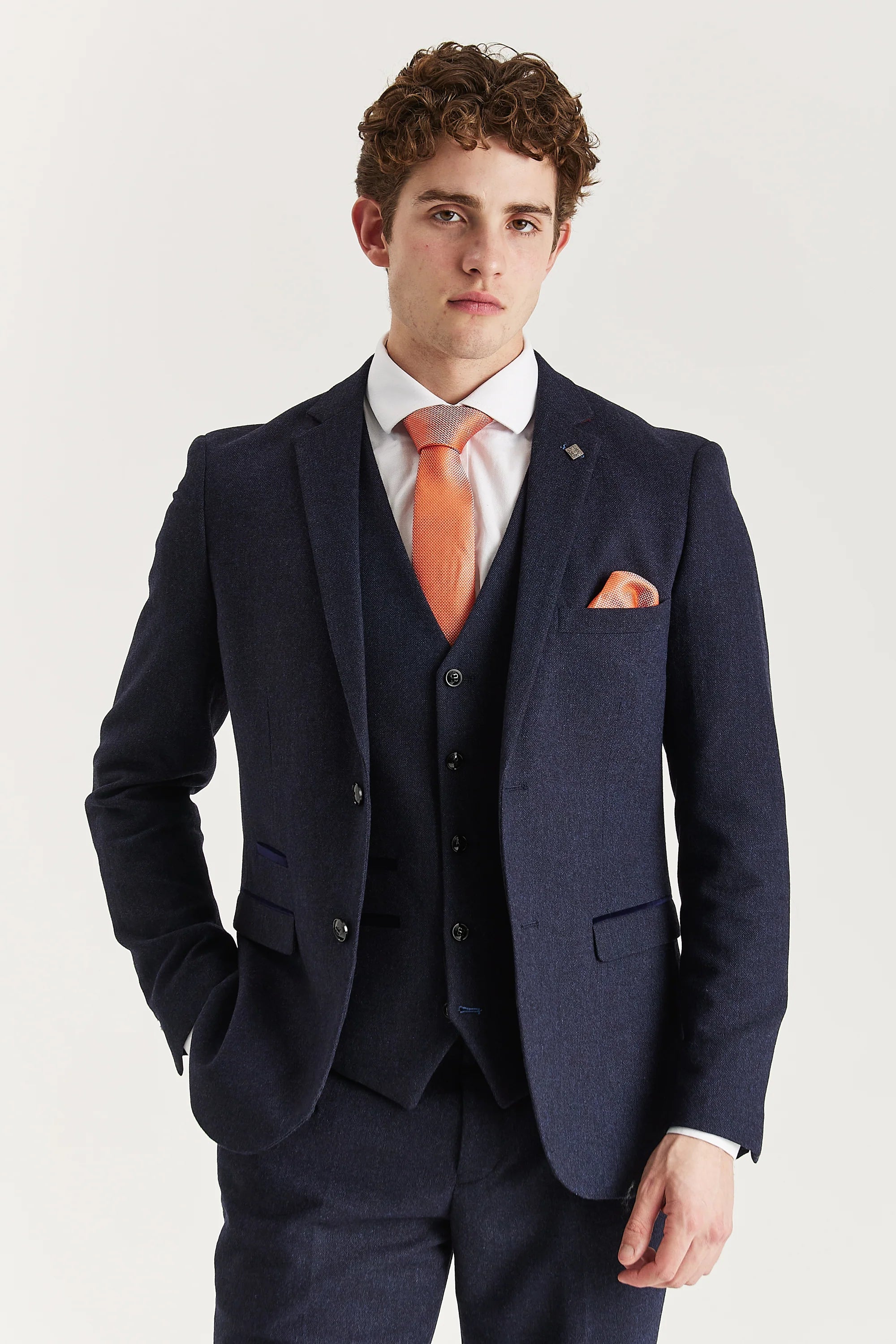 Close-up of Oscar navy tweed three-piece suit jacket with matching waistcoat, white shirt, and orange tie and pocket square.