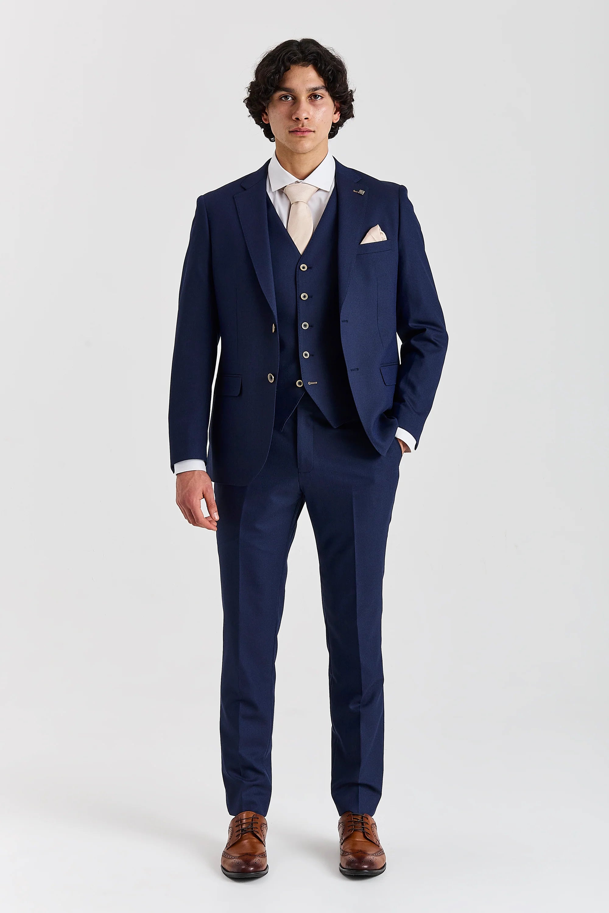 Full-length front view of a man wearing a Belmont navy three piece suit with cream tie, pocket square and brown shoes.