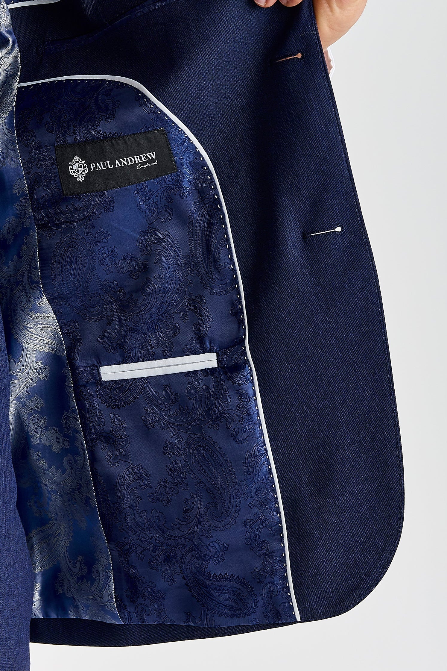 Detail view of a Belmont navy suit jacket interior with blue paisley lining, white piping, inner pocket and Paul Andrew label.