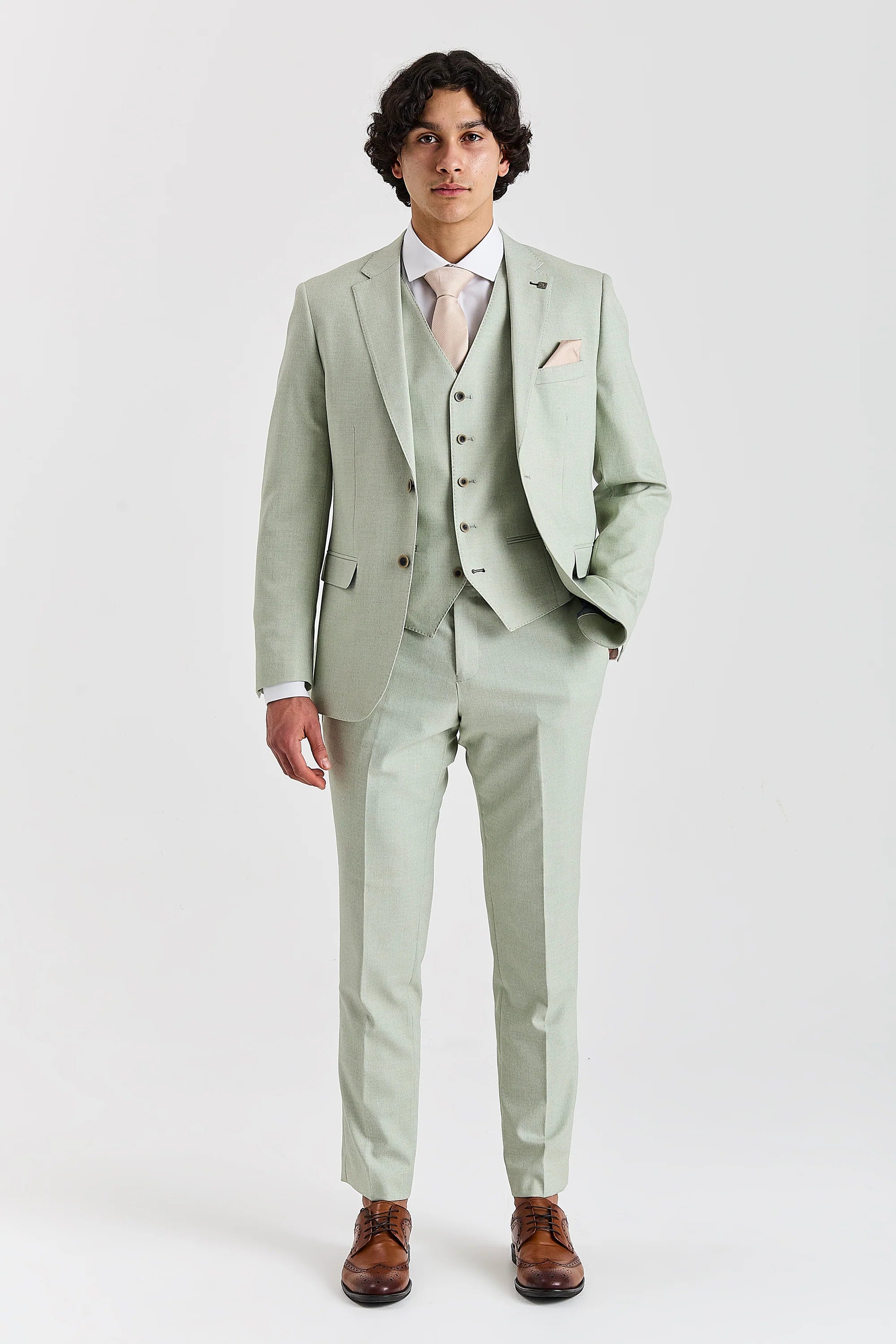 Full-length front view of a man wearing a mint green three piece suit with a cream tie, white shirt and brown brogue shoes.