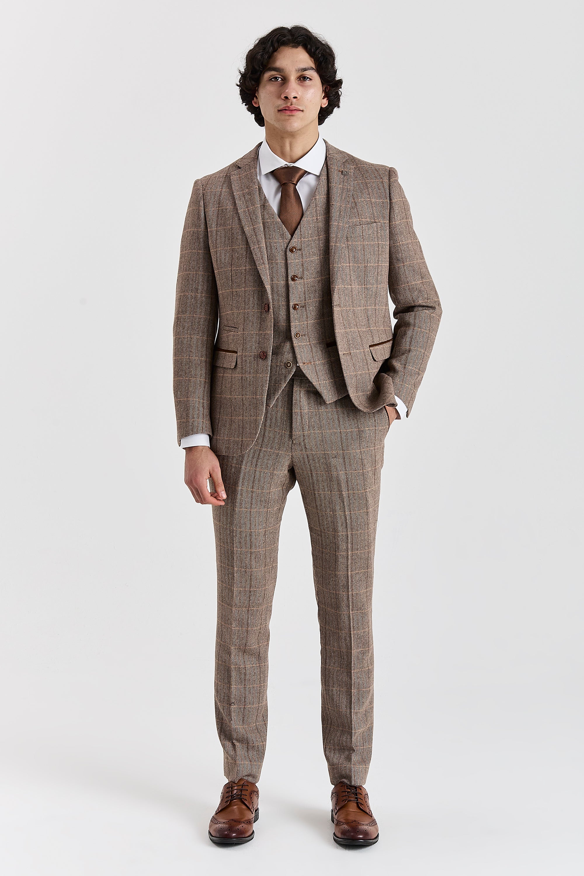 Full-length front view of a man wearing a Harris brown herringbone tweed check three piece suit with brown tie and brown shoes.