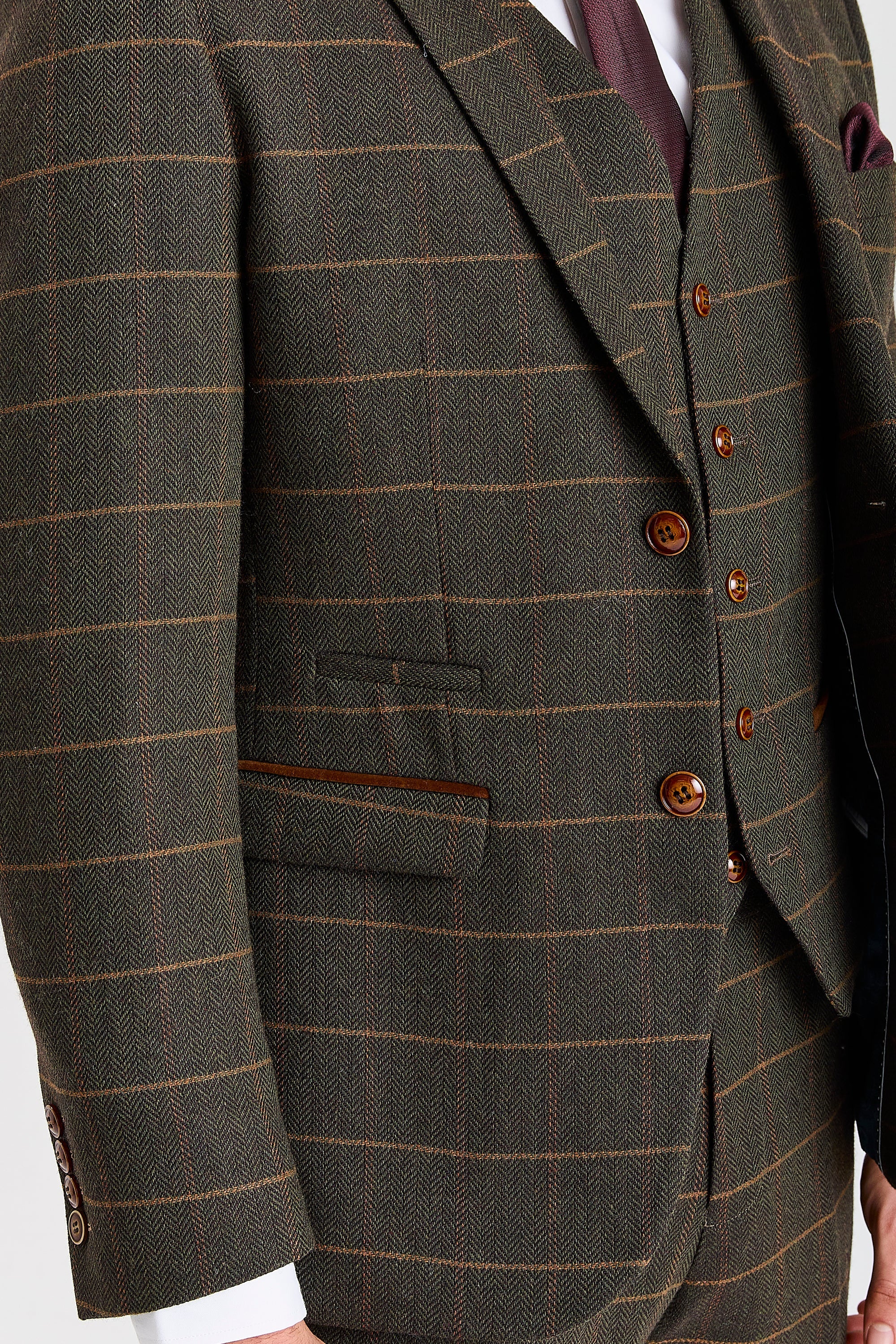 Close-up of a Harris green herringbone tweed suit jacket and waistcoat with a tan windowpane check, brown buttons and brown trim detail.