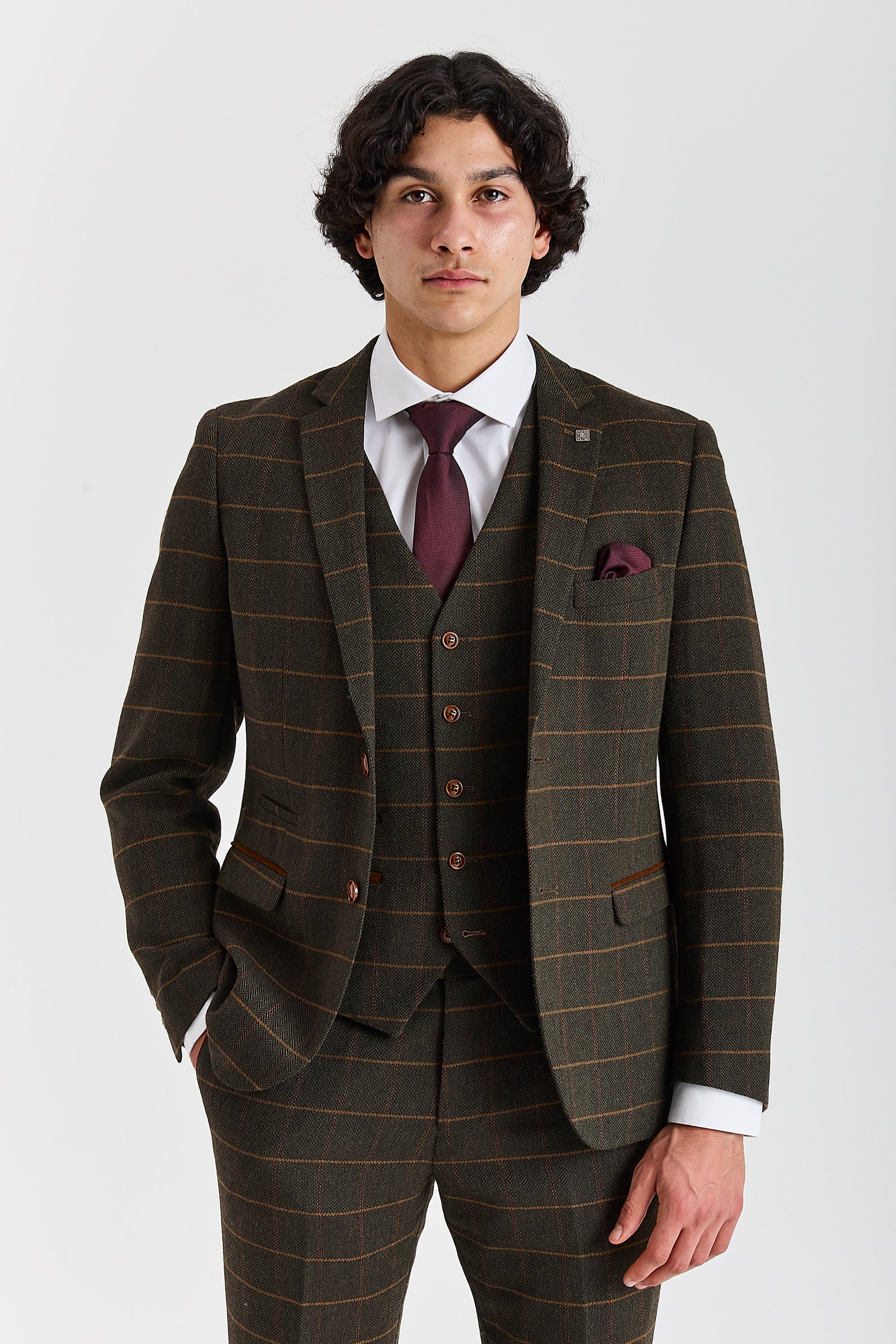 Front view of a man wearing a Harris green herringbone tweed three piece suit with a tan windowpane check, burgundy tie and matching waistcoat.