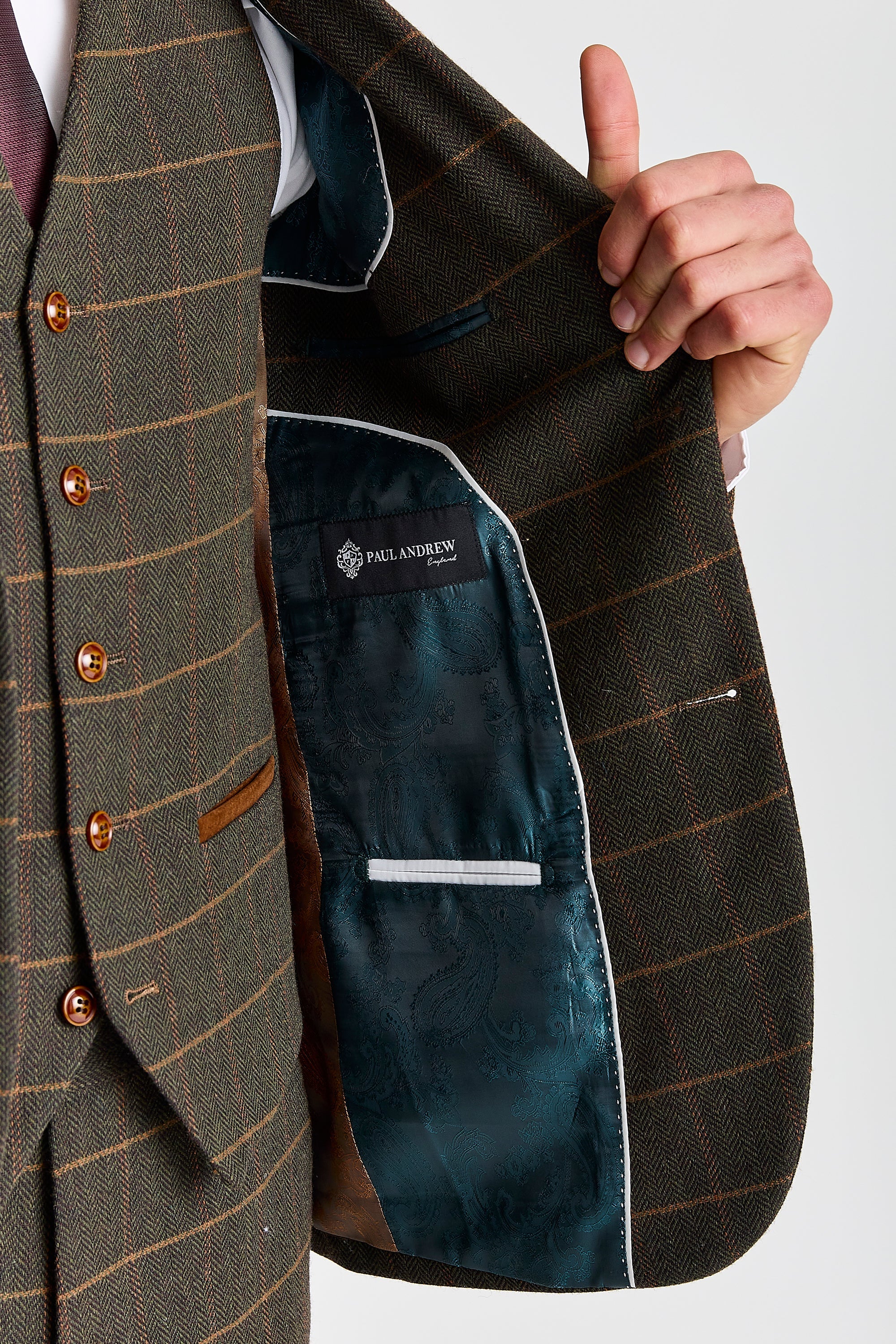 Detail view of a Harris green herringbone tweed suit jacket with tan windowpane check, showing green paisley lining, inner pocket and Paul Andrew label.