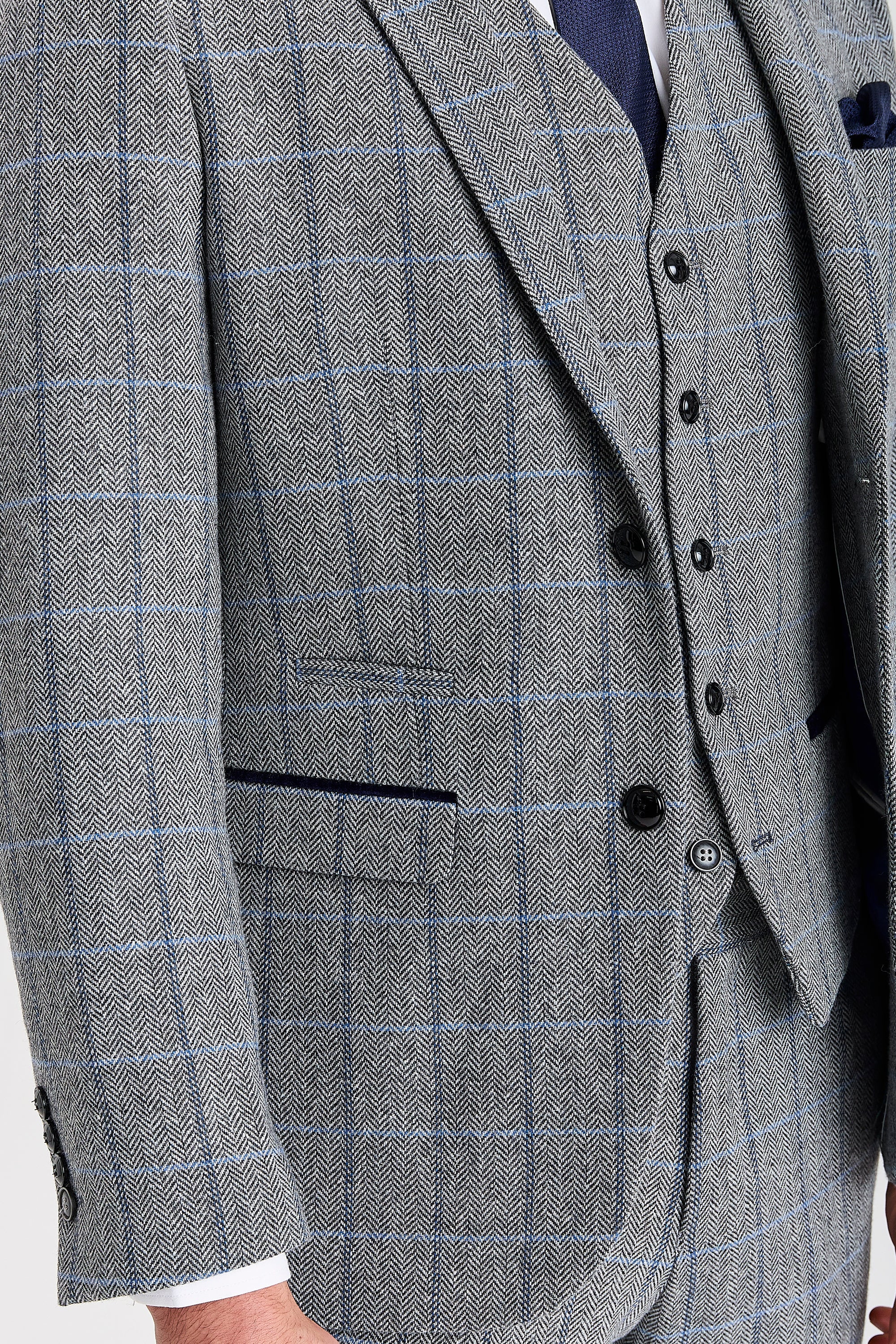 Close-up detail of a Harris grey herringbone tweed check suit jacket and waistcoat with black buttons, blue windowpane check and suede pocket trims.