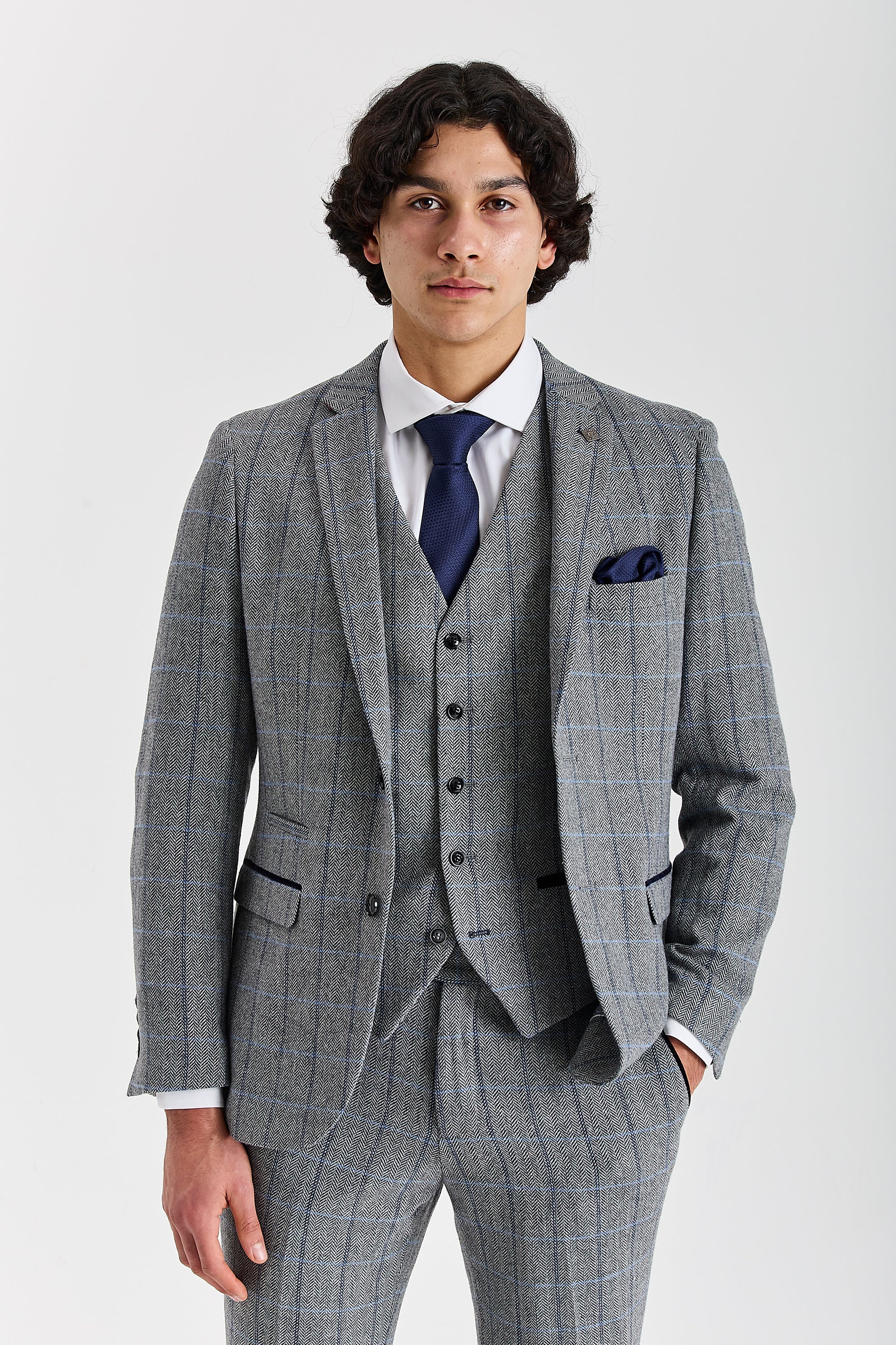 Front view of a man wearing a Harris grey herringbone tweed check three piece suit with waistcoat, trousers, white shirt and navy tie.