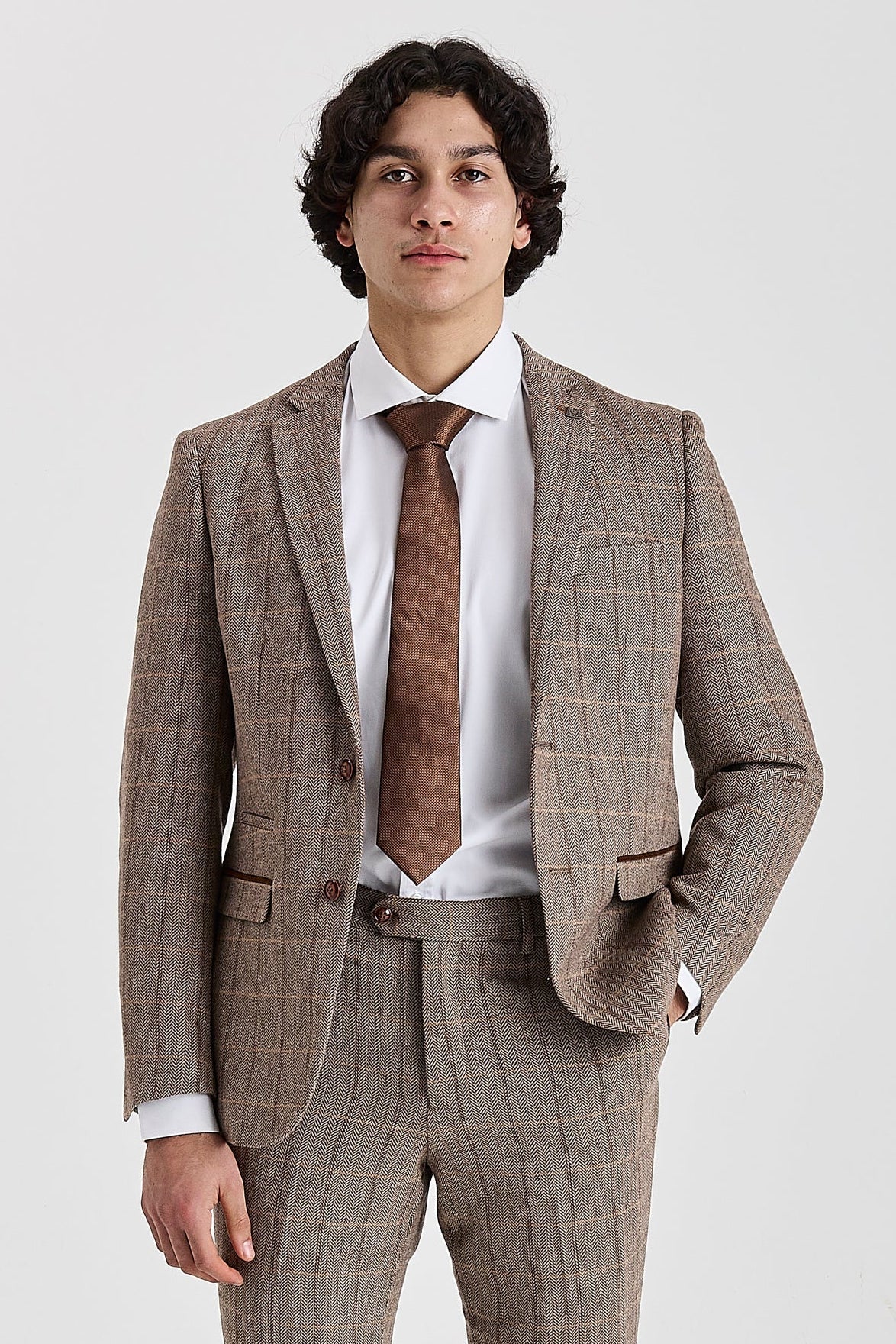 Knee-up front view of a man wearing a tailored brown herringbone tweed suit jacket with a windowpane check pattern, styled with a white shirt and a brown tie