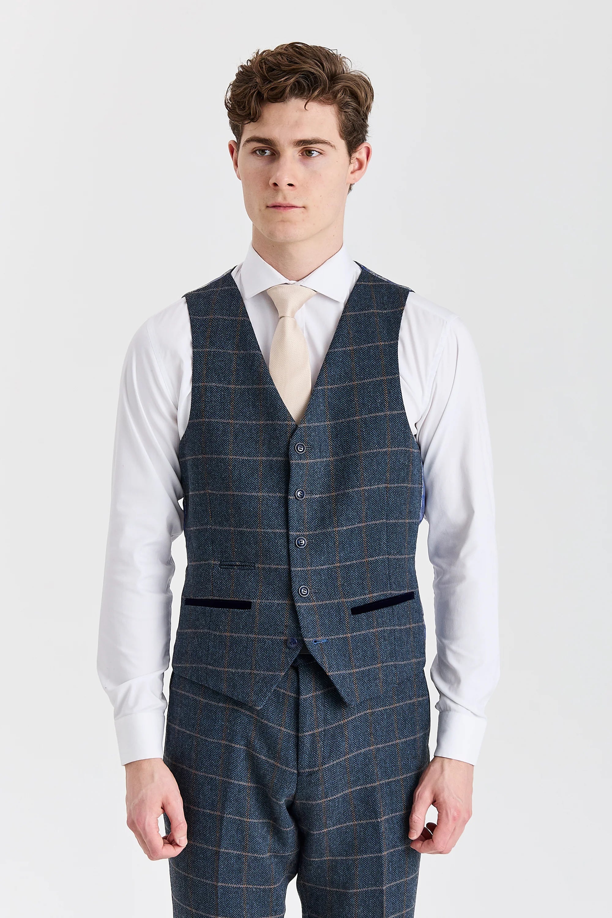 Front view of the navy herringbone tweed waistcoat with contrast pocket trimmings, worn with matching trousers, a white shirt and a cream tie.