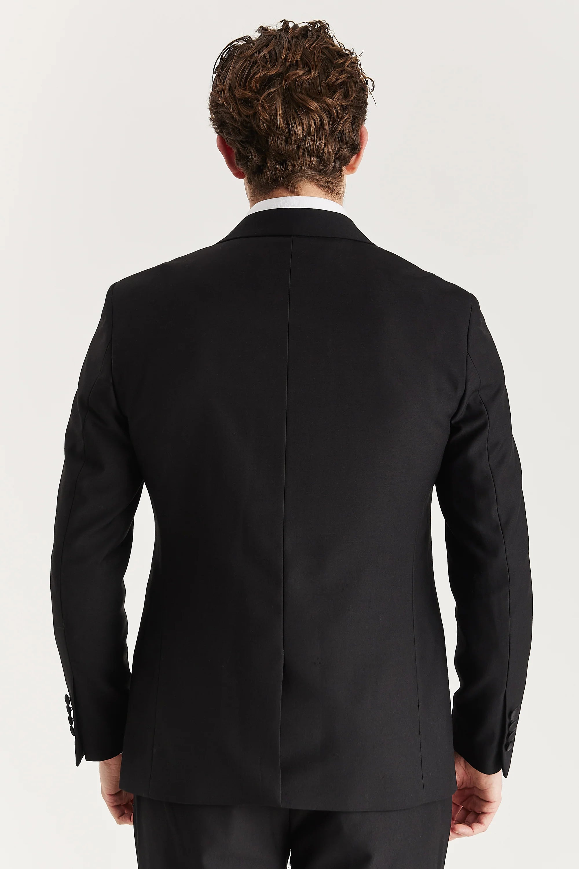 Back view of a black dinner suit jacket with matching trousers.