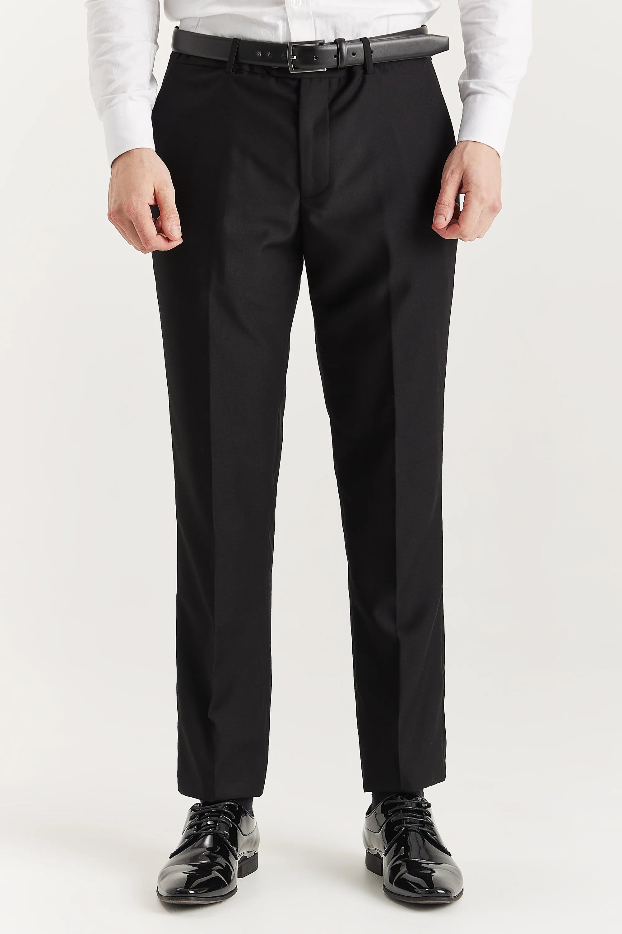 Front view of black trousers, shown with a black belt, white shirt cuffs and black shoes.