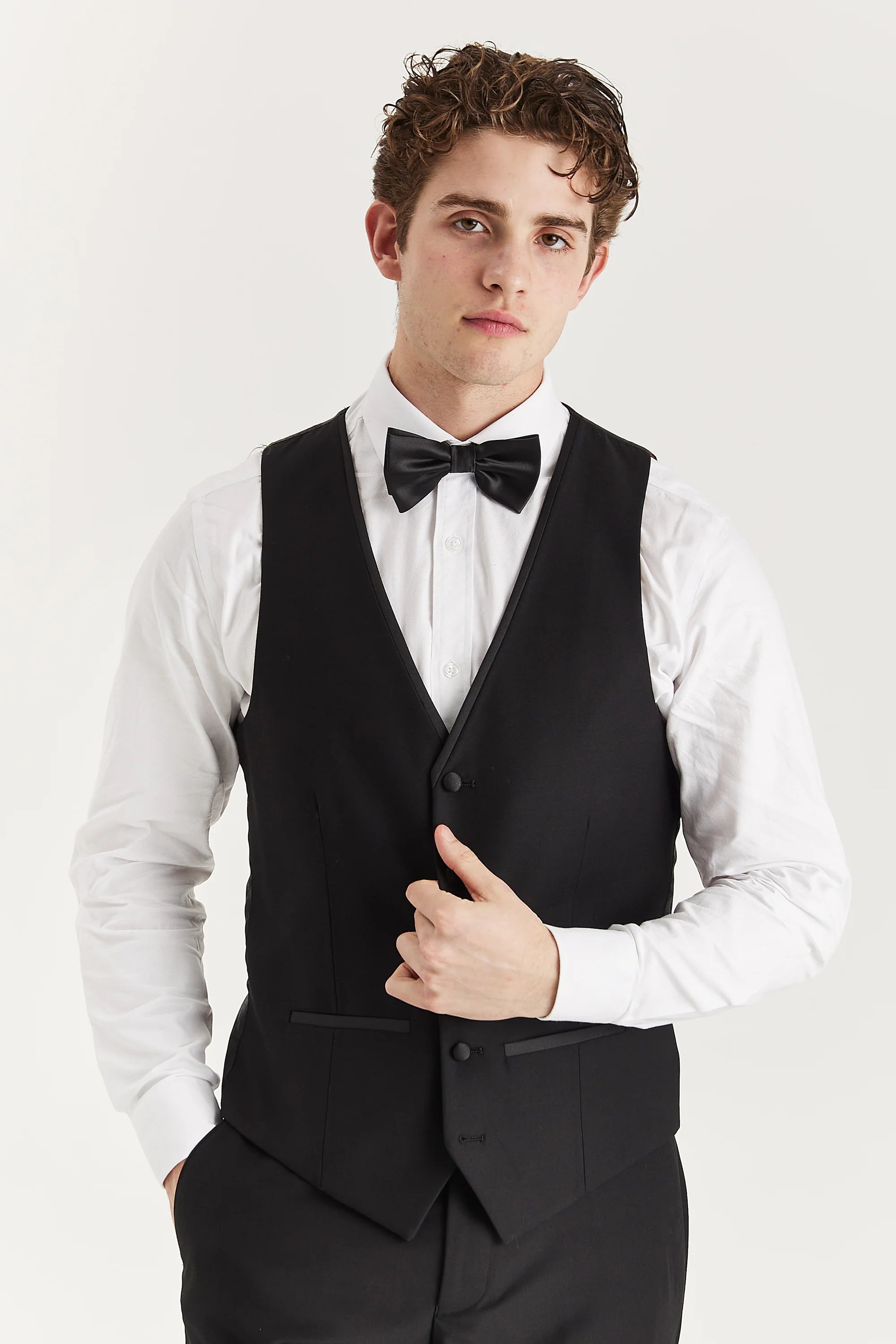 Front view of a black waistcoat with matching trousers, a white shirt and a black bow tie.