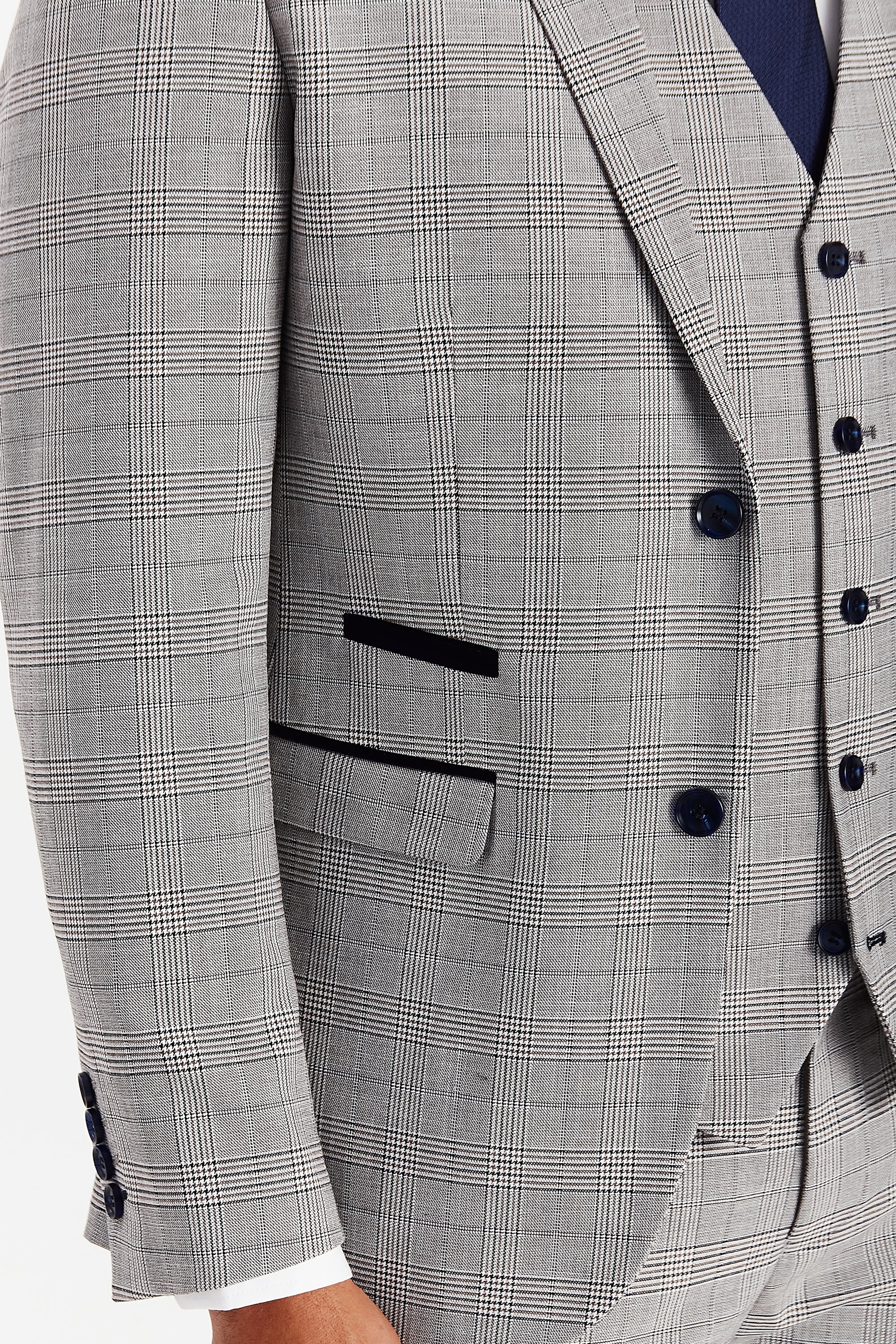 Detail view of grey glen check jacket and waistcoat fabric with navy buttons and dark navy pocket trim.