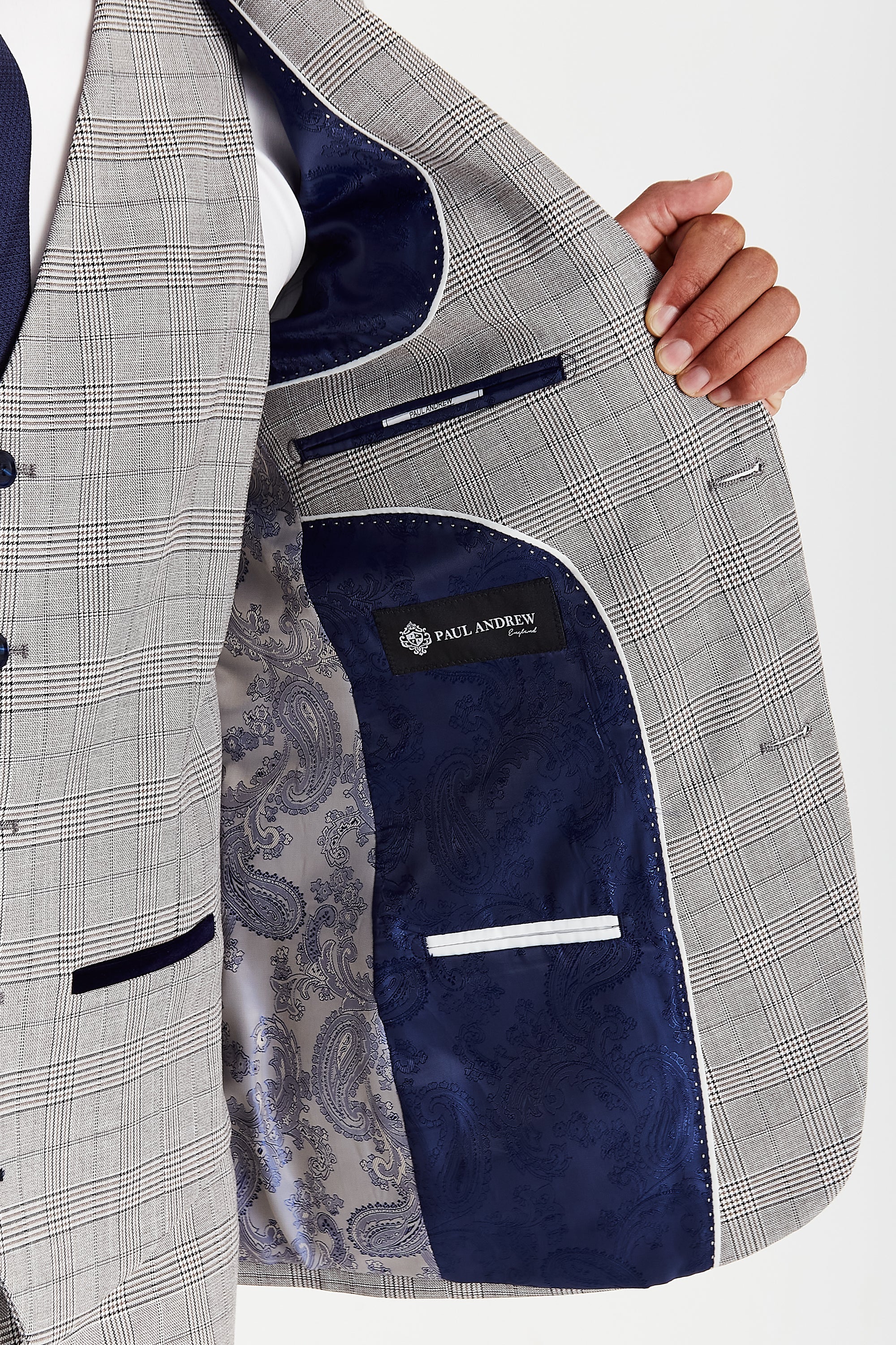 Detail view of a grey glen check suit jacket interior with navy paisley lining, white piping, inner pockets and a Paul Andrew label.