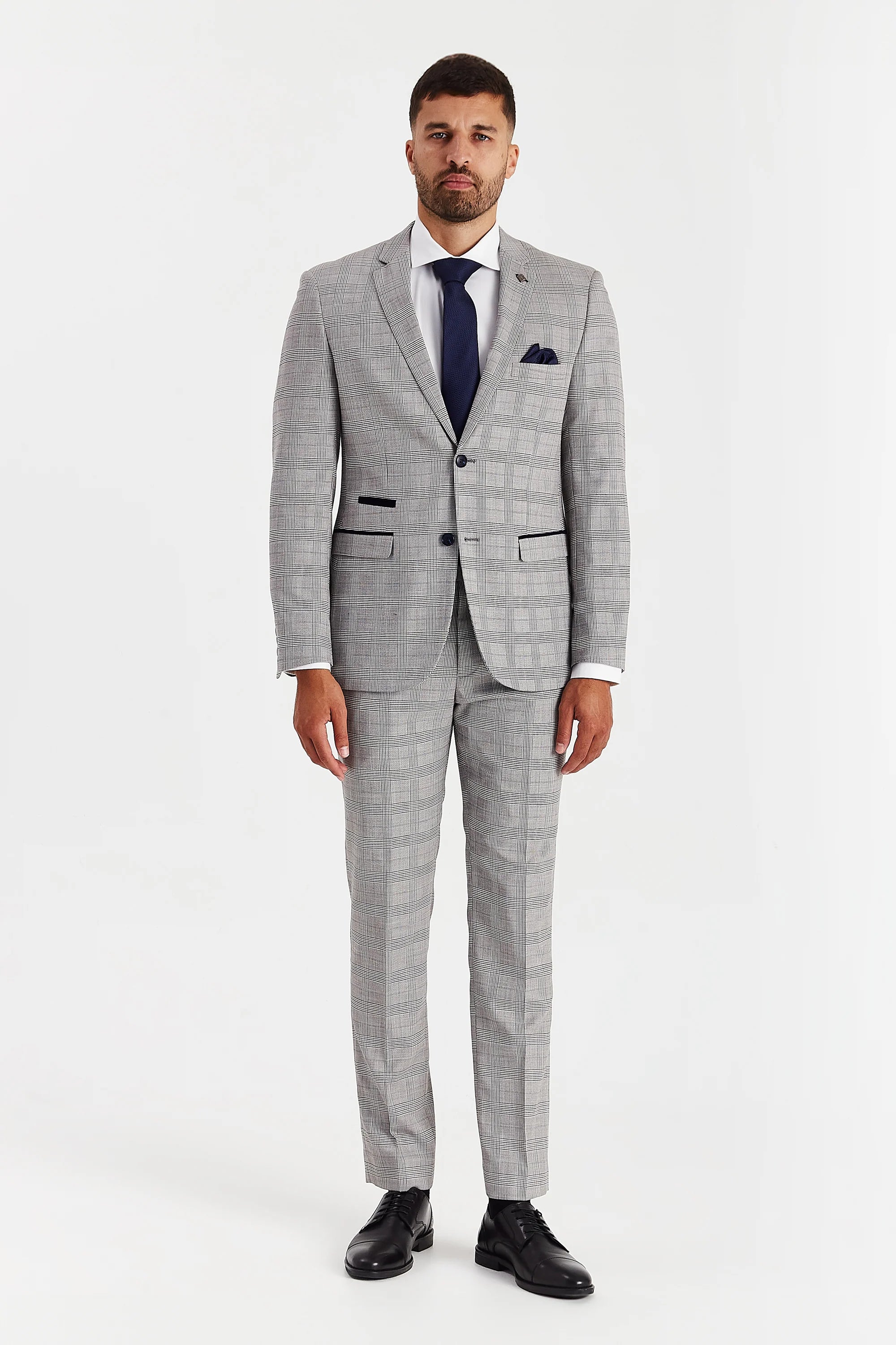 Full-length front view of a man in a grey windowpane check two-piece suit, styled with a navy tie and black shoes.