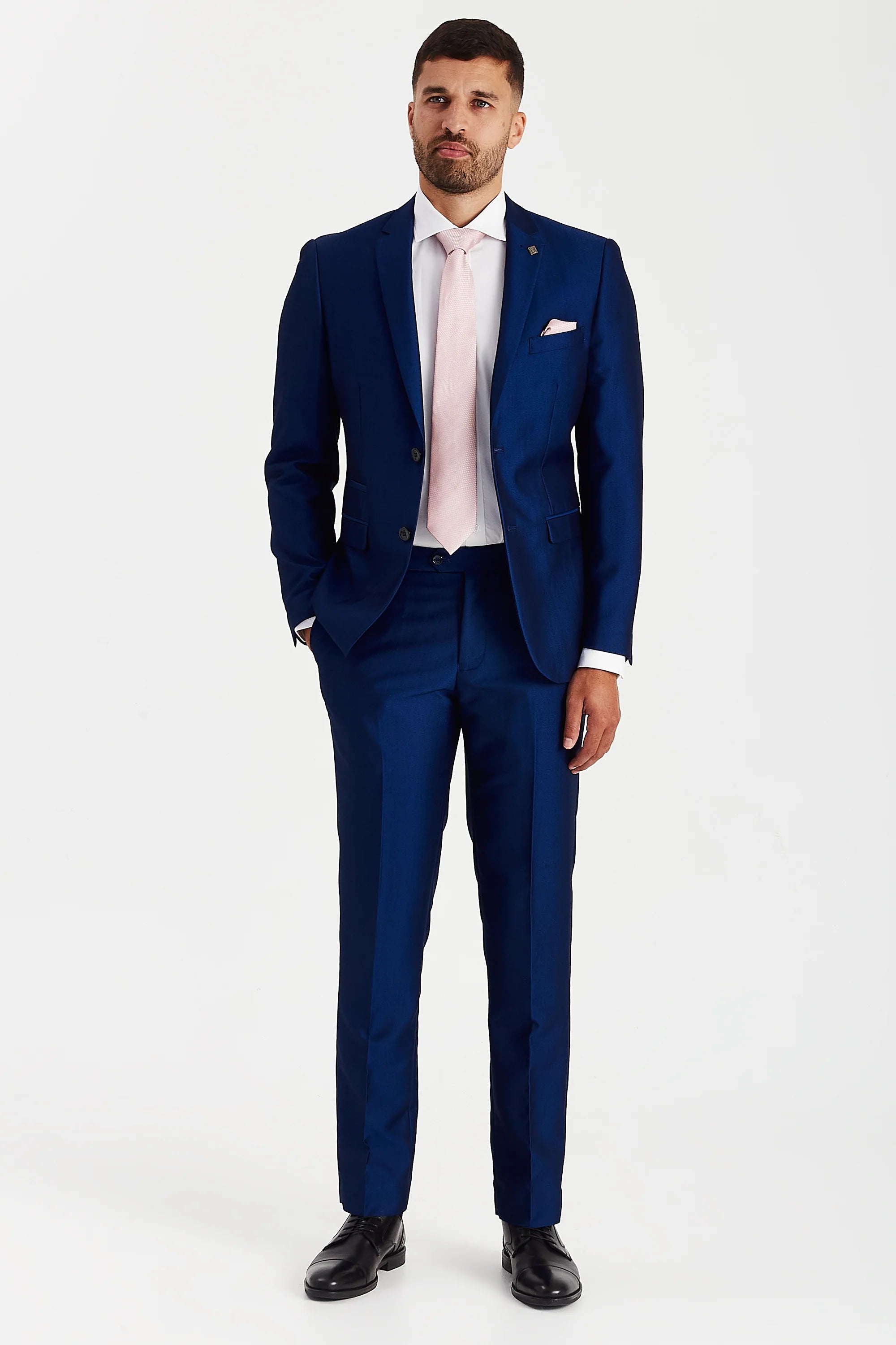 Full-length view of a man modeling a glossy blue two-piece suit with a white shirt, light pink tie, and black leather shoes.