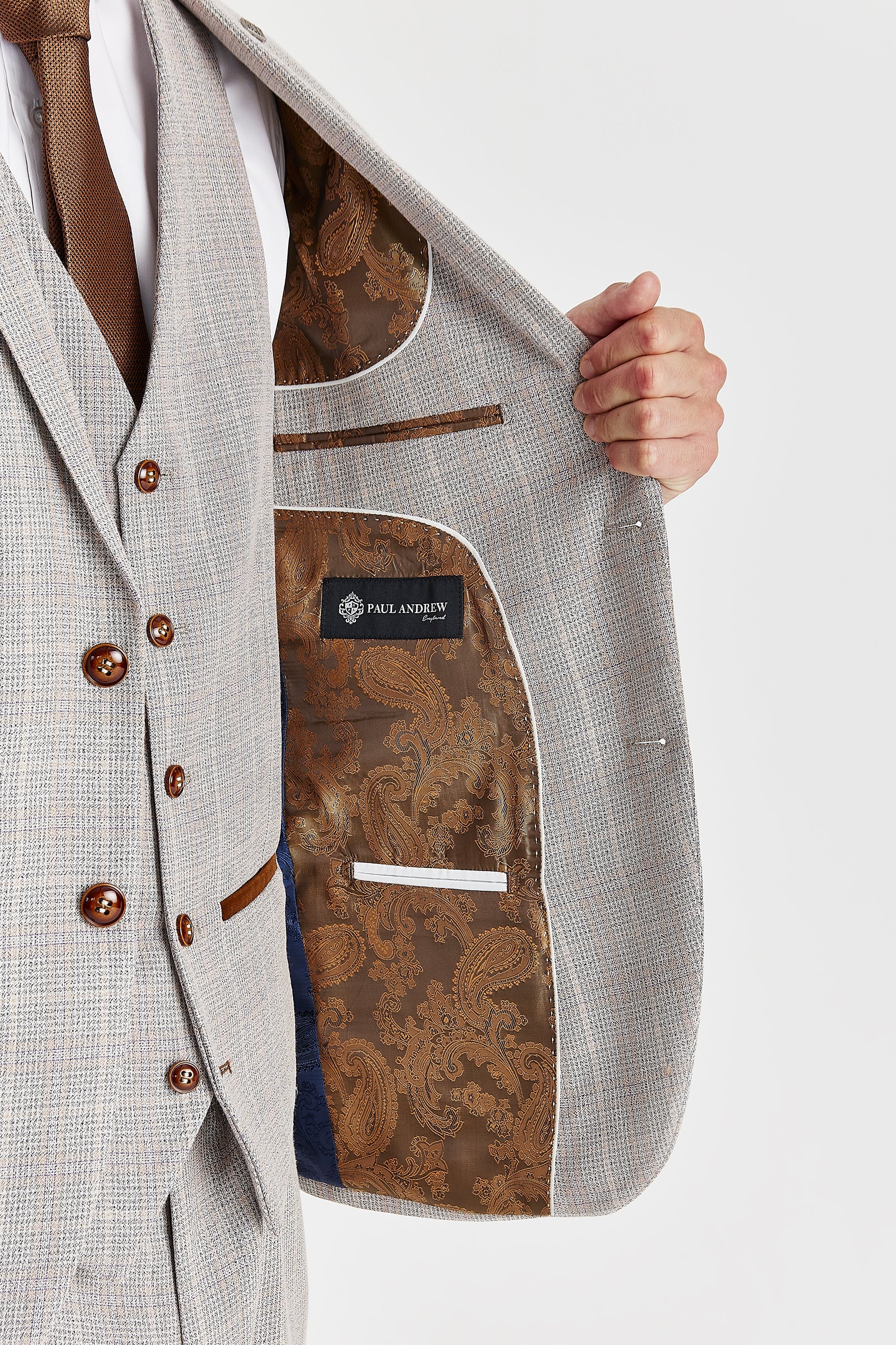 Detail view of a beige check suit jacket interior with brown paisley lining, white piping, inner pockets and a Paul Andrew label.