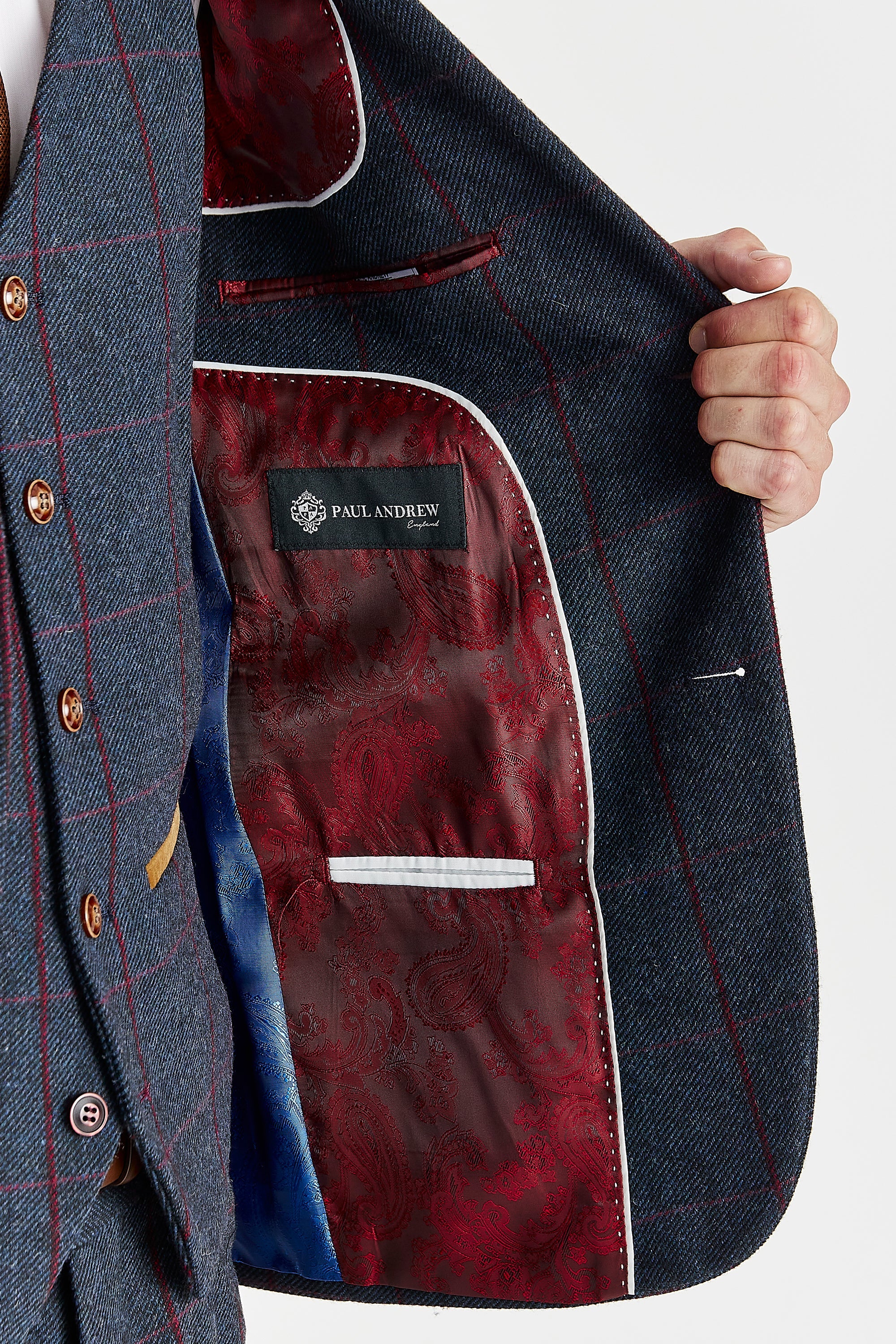 Detail view of a navy tweed suit jacket interior with red paisley lining, white piping, inner pockets and a Paul Andrew label.