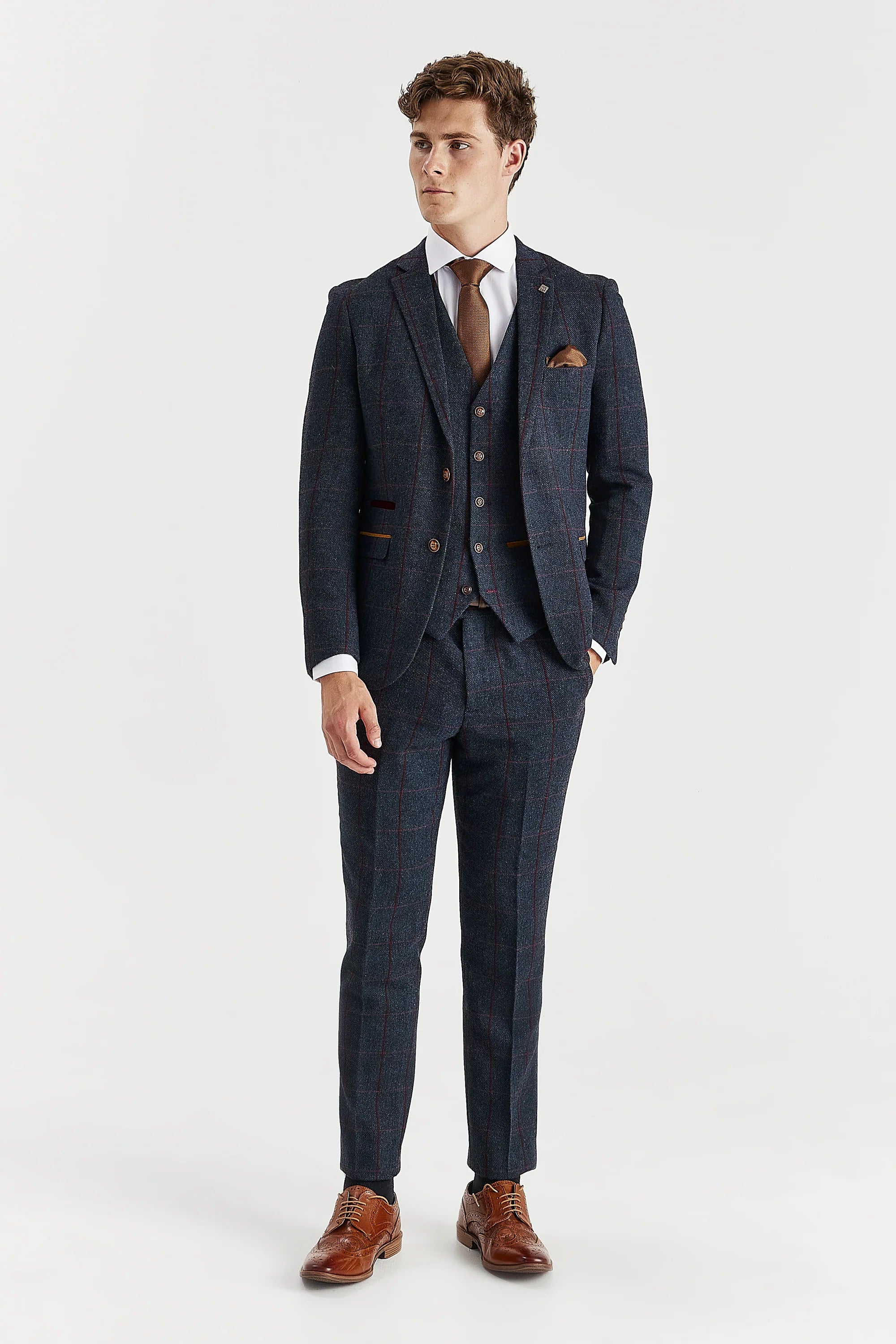 Full-length front view of a man wearing a navy tweed three piece suit with a burgundy windowpane check pattern, jacket, waistcoat, trousers, white shirt, brown tie and brown shoes.