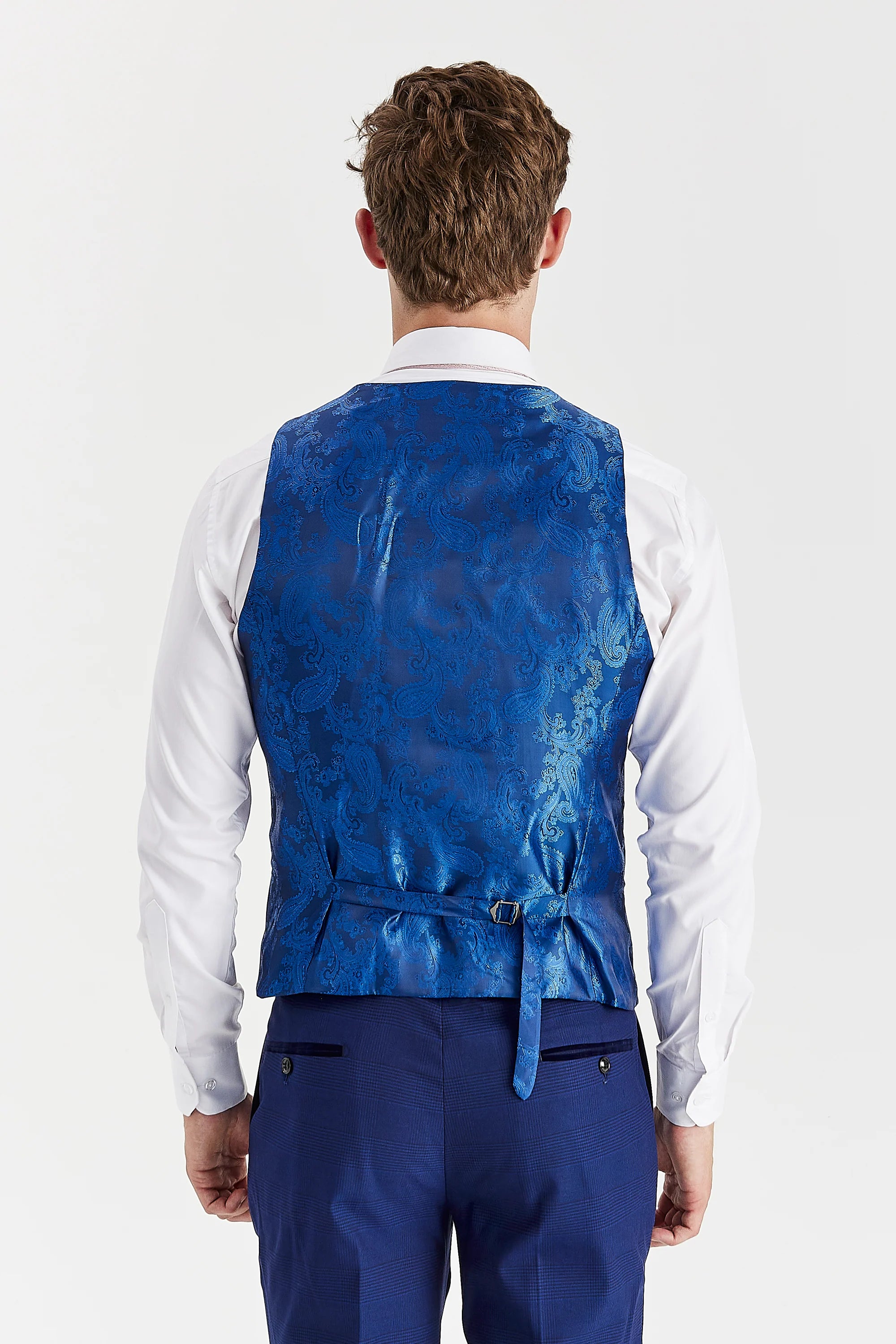 Rear view of the blue waistcoat with a blue paisley back panel and adjustable strap, worn with a white shirt and matching trousers.