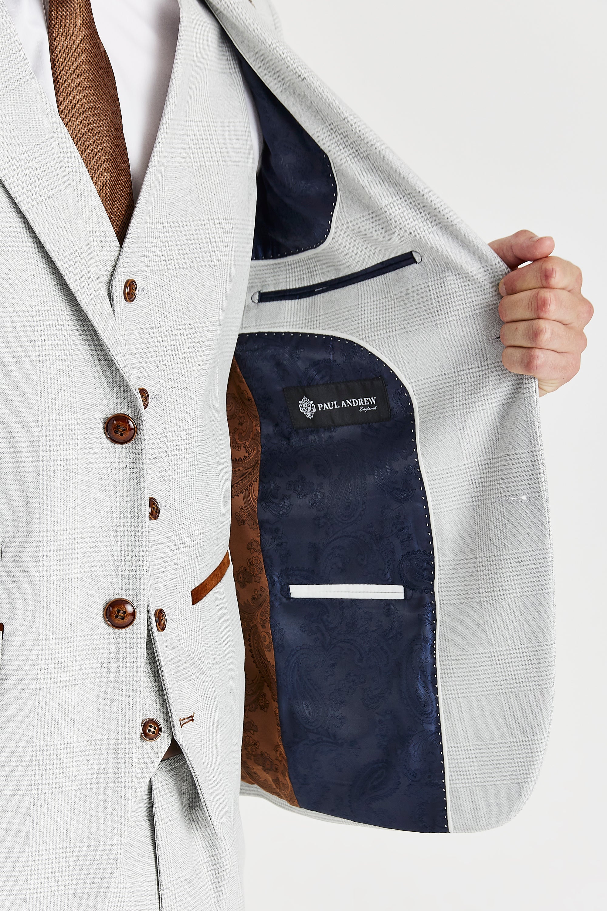 Detail view of a stone glen check suit jacket interior with navy and brown paisley lining, white piping, inner pockets and a Paul Andrew label.