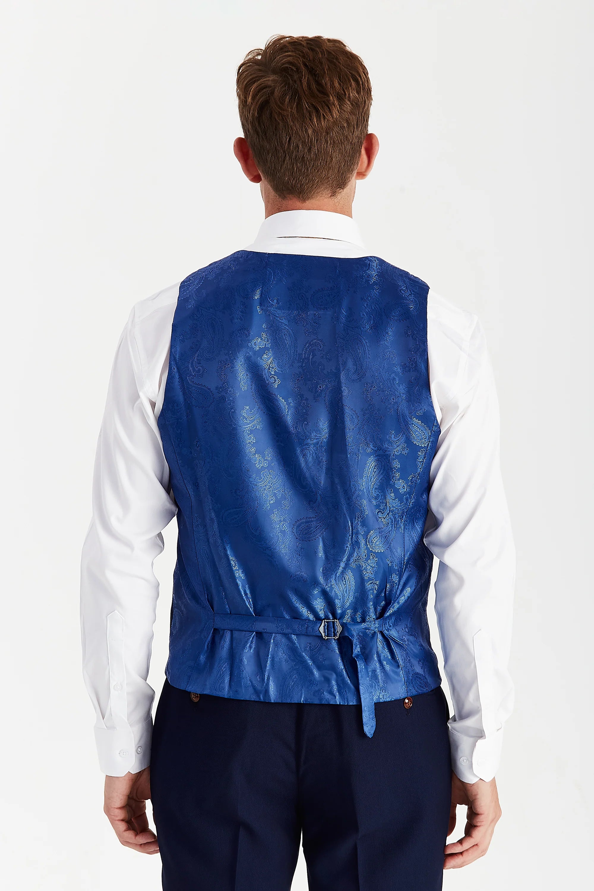 Back view of a blue paisley waistcoat panel with an adjustable strap, worn with navy trousers and a white shirt.
