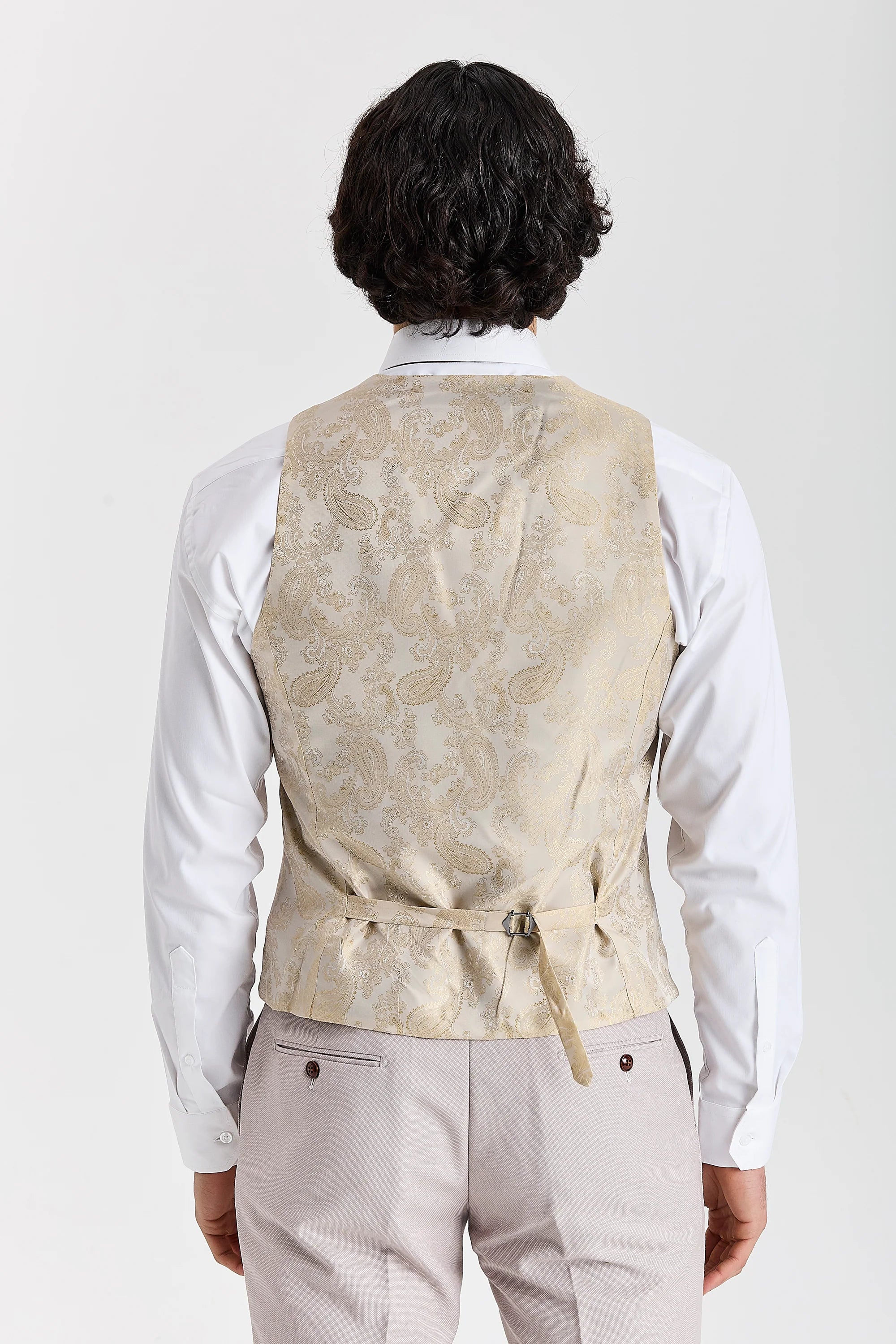 Back view of a gold paisley waistcoat panel with an adjustable strap, worn with stone textured trousers and a white shirt.