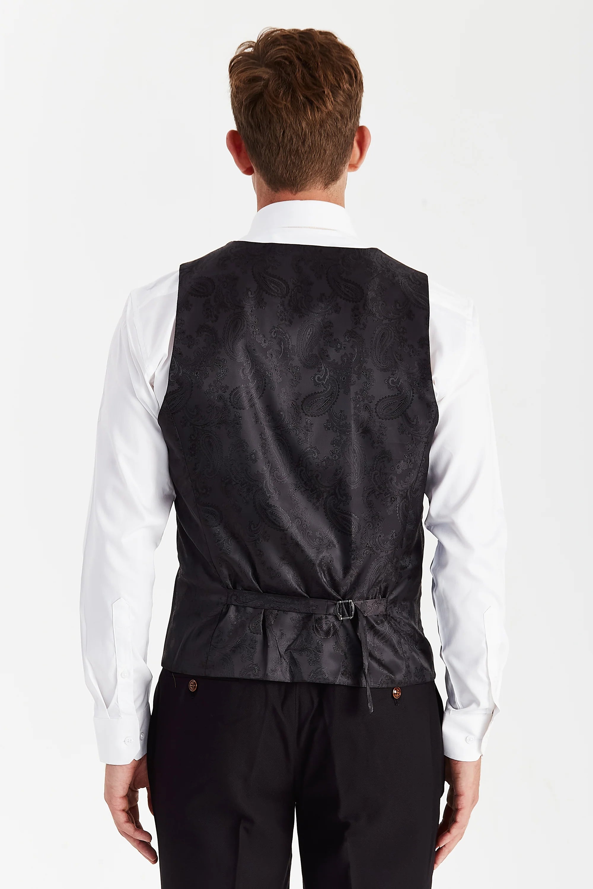 Rear view of the black waistcoat with a black paisley back panel and adjustable strap, worn with a white shirt and black trousers